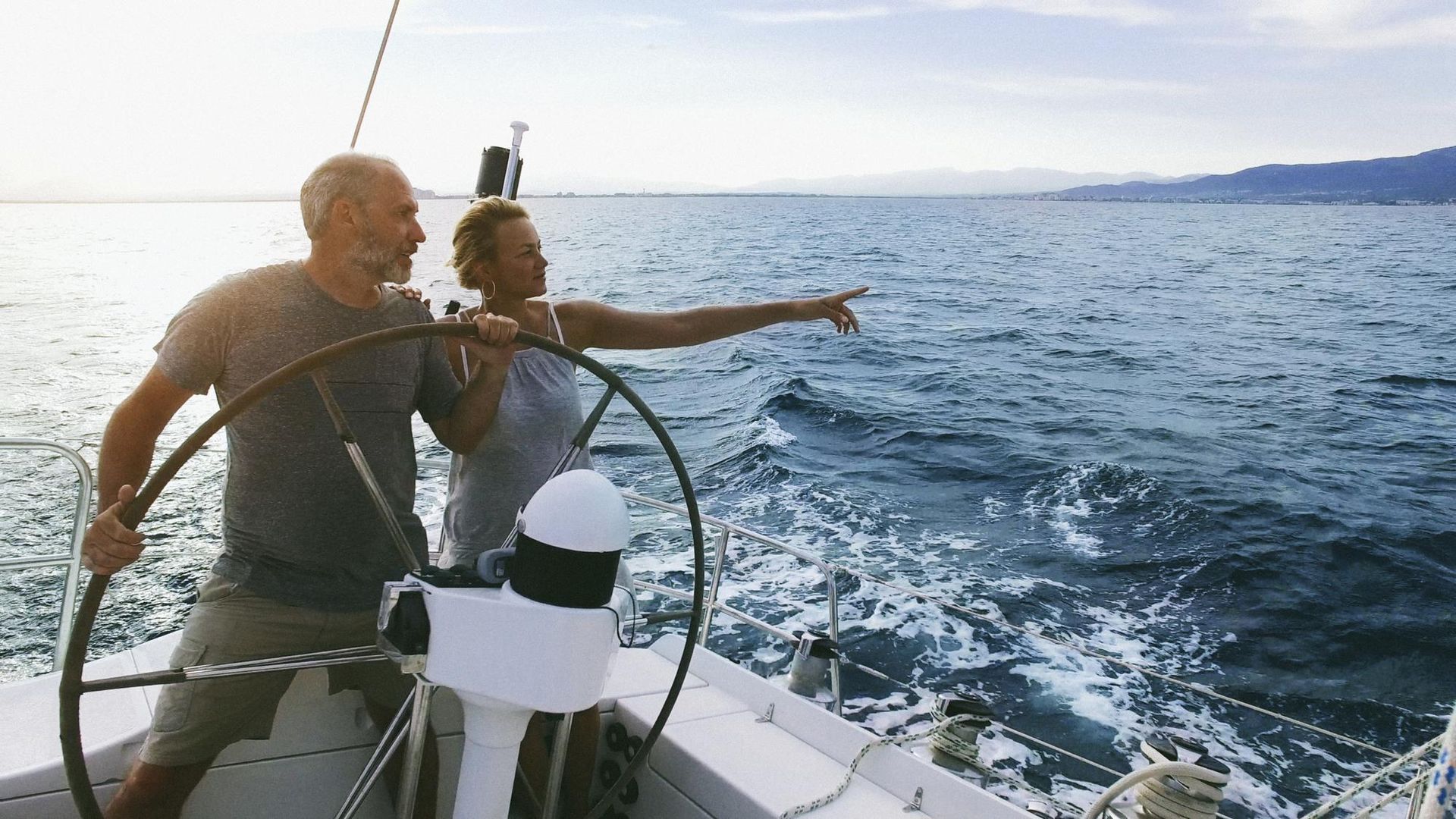 Two people on a sailboat pointing across the ocean at sunset