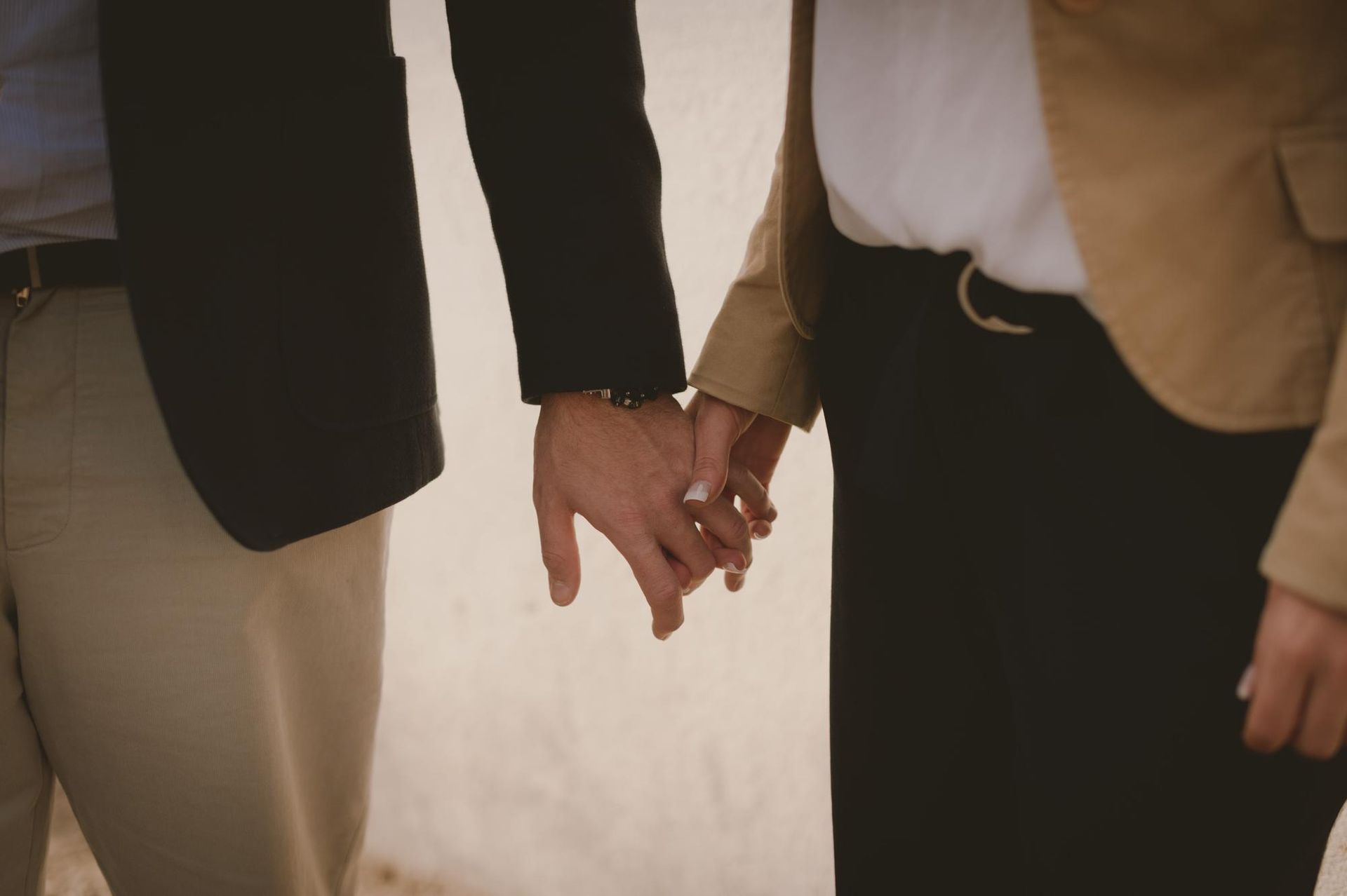 Two people holding hands outdoors, wearing black and tan jackets.