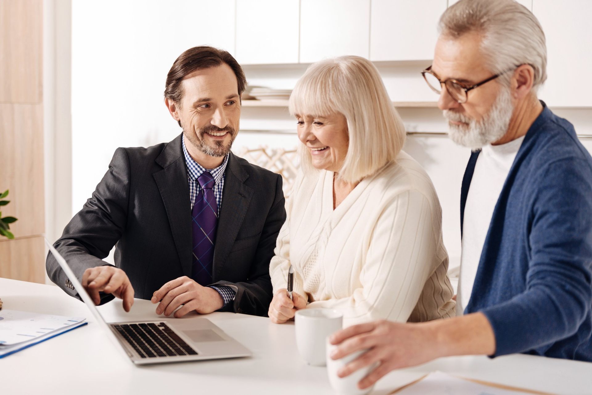 Three people discussing documents at a laptop in a bright office