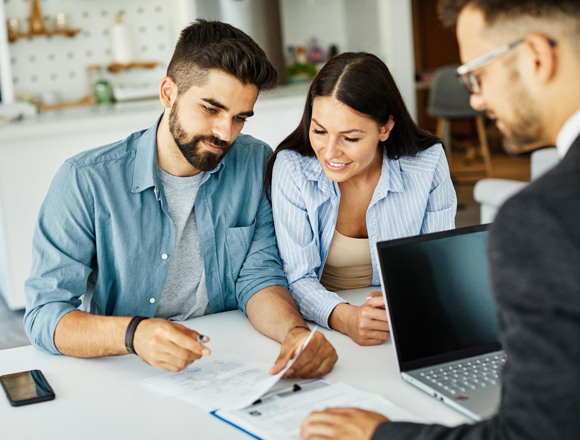 Three people reviewing documents at a table beside a laptop in a bright office