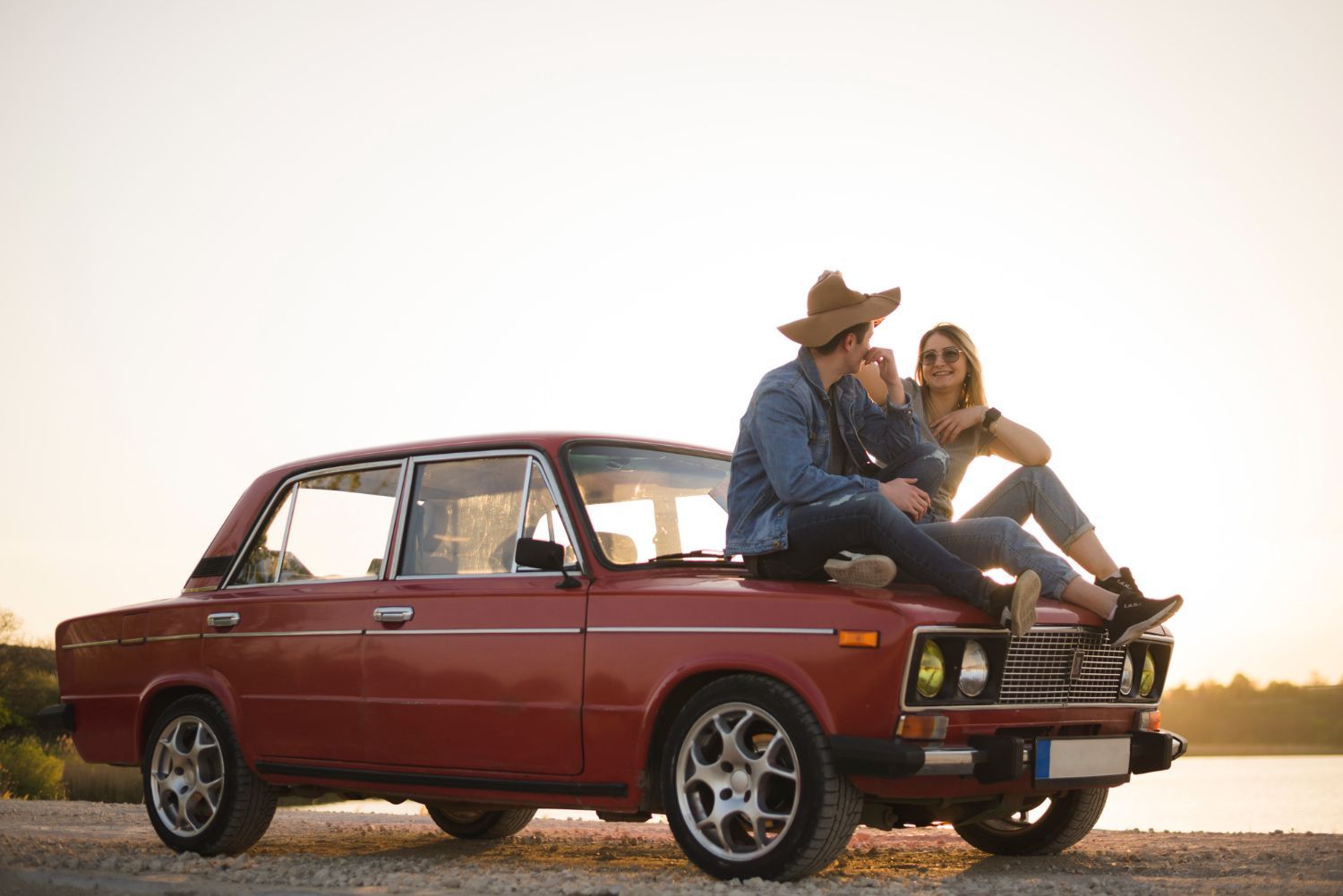 Two people sitting on a red vintage car at sunset