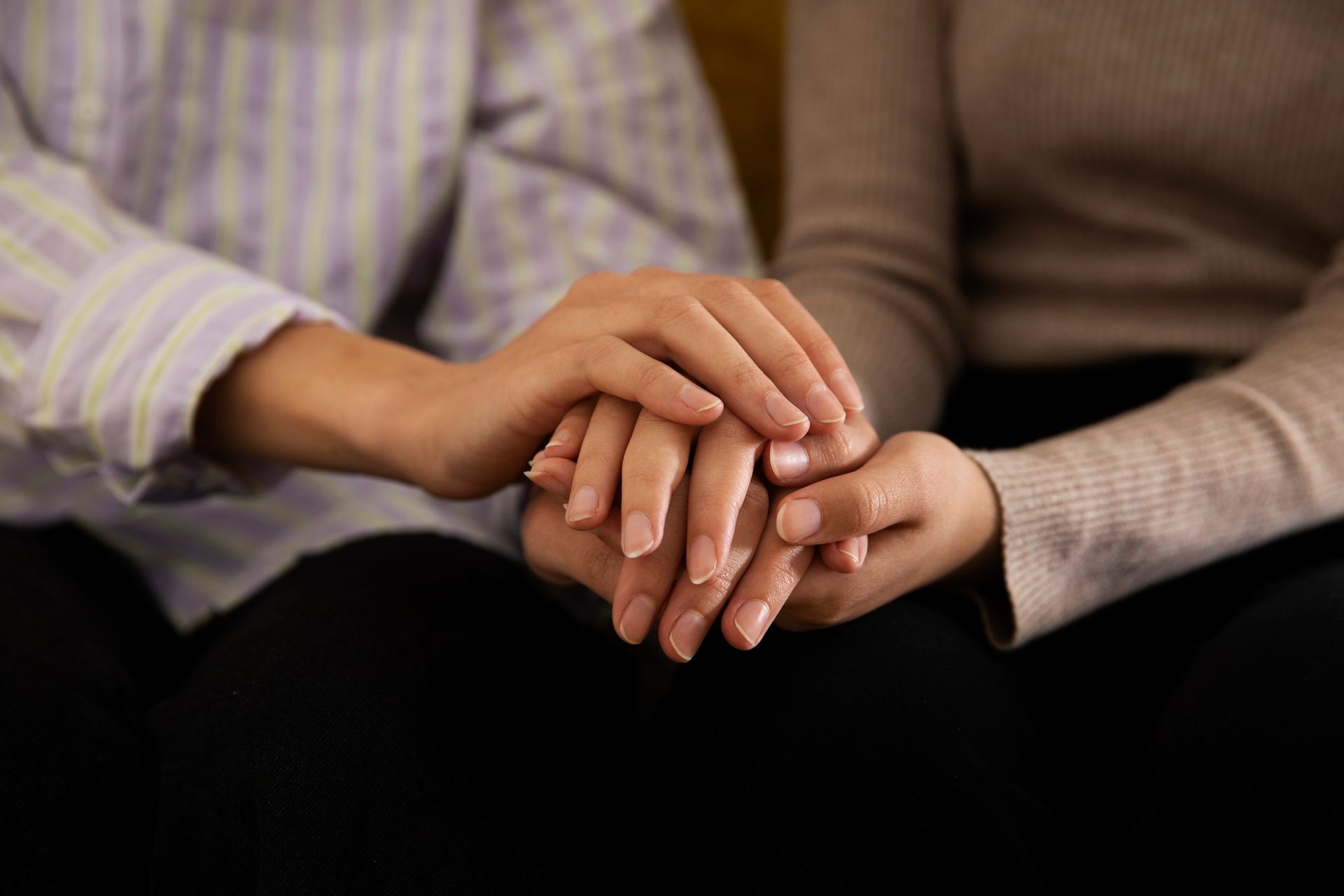 Two people holding hands in a supportive gesture, seated closely together