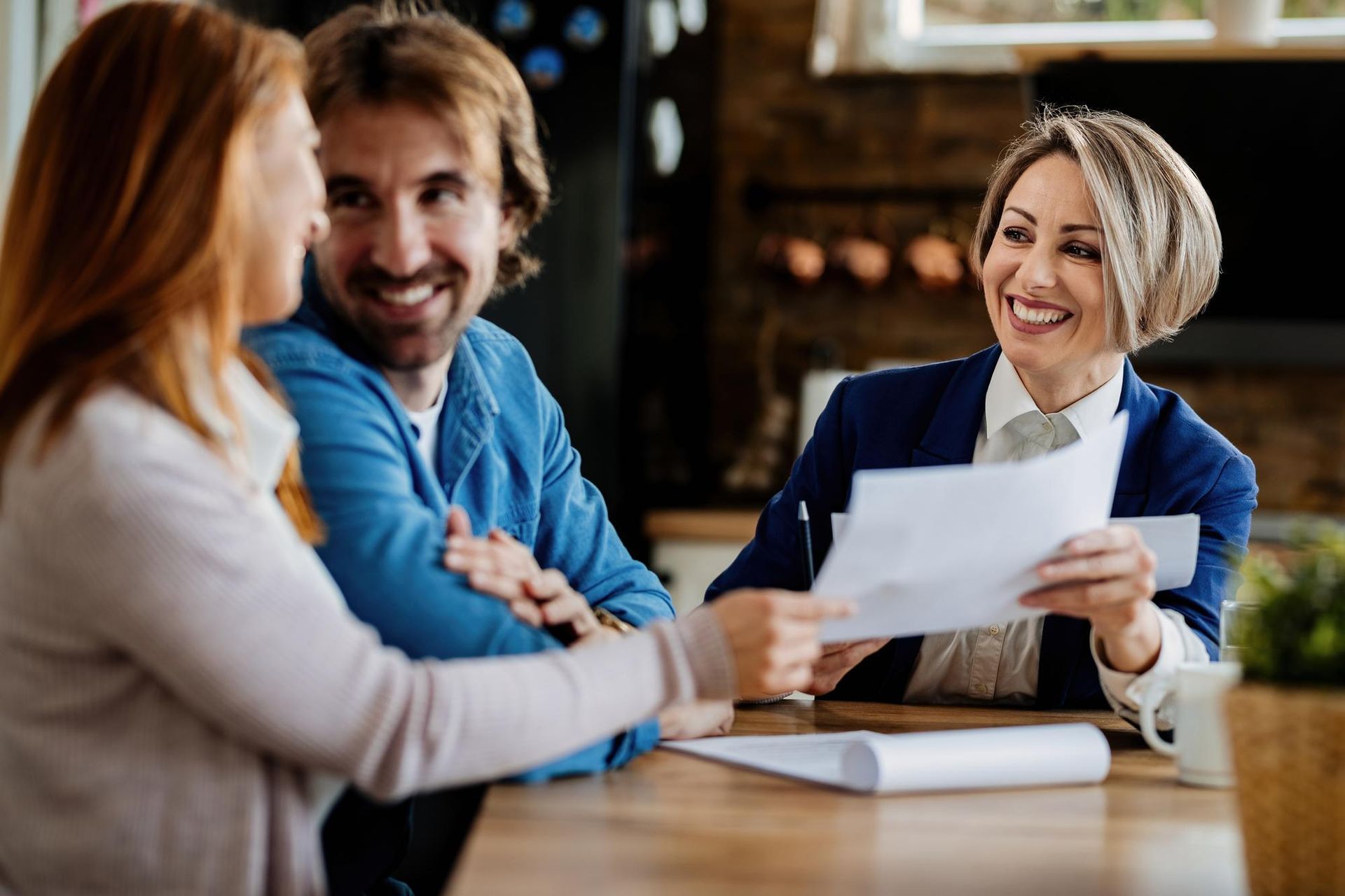 Three people smiling and talking at a table, reviewing a document in a warm office setting