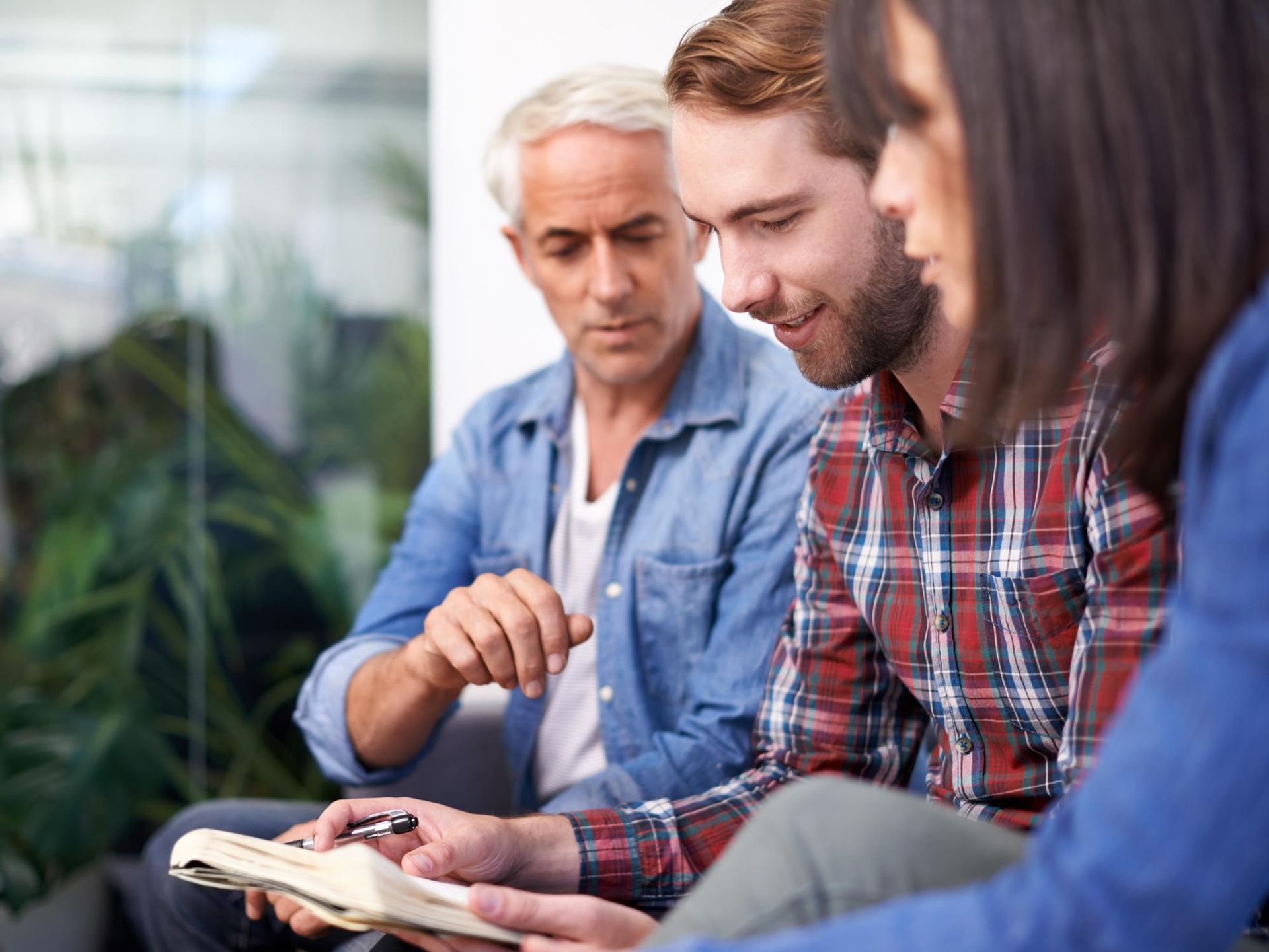 Three people sitting together, discussing a notebook outdoors in a relaxed setting