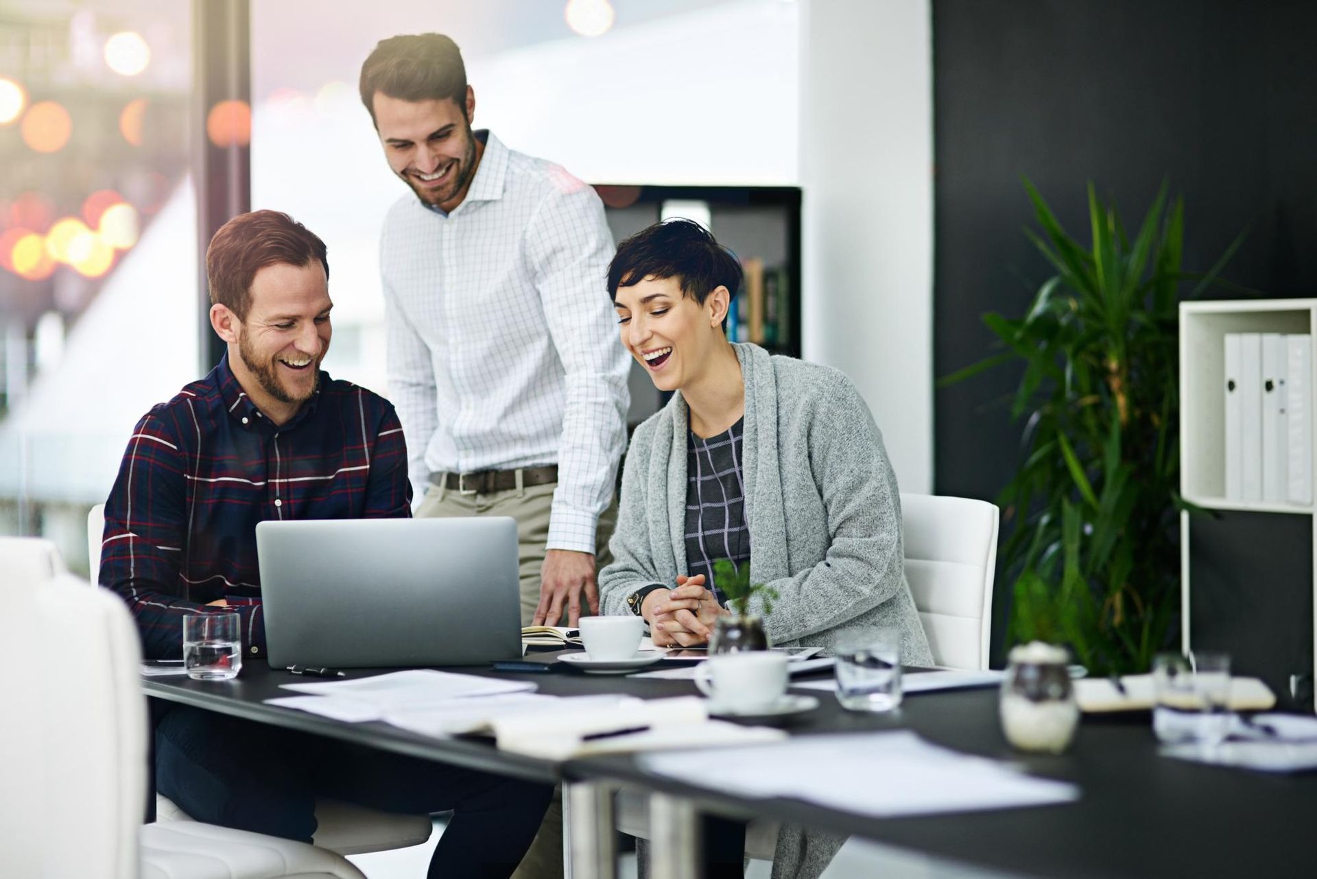 Three coworkers reviewing a laptop in a bright office meeting space