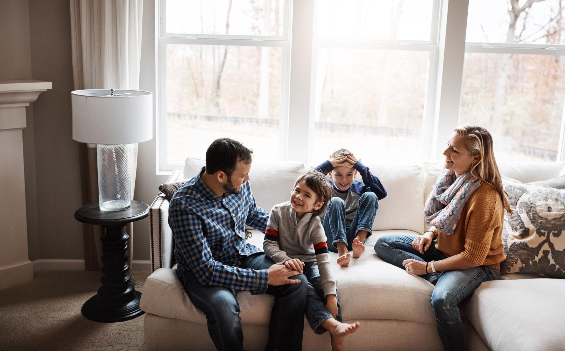 Family sitting on a couch in a bright living room, chatting with a child and a dog nearby