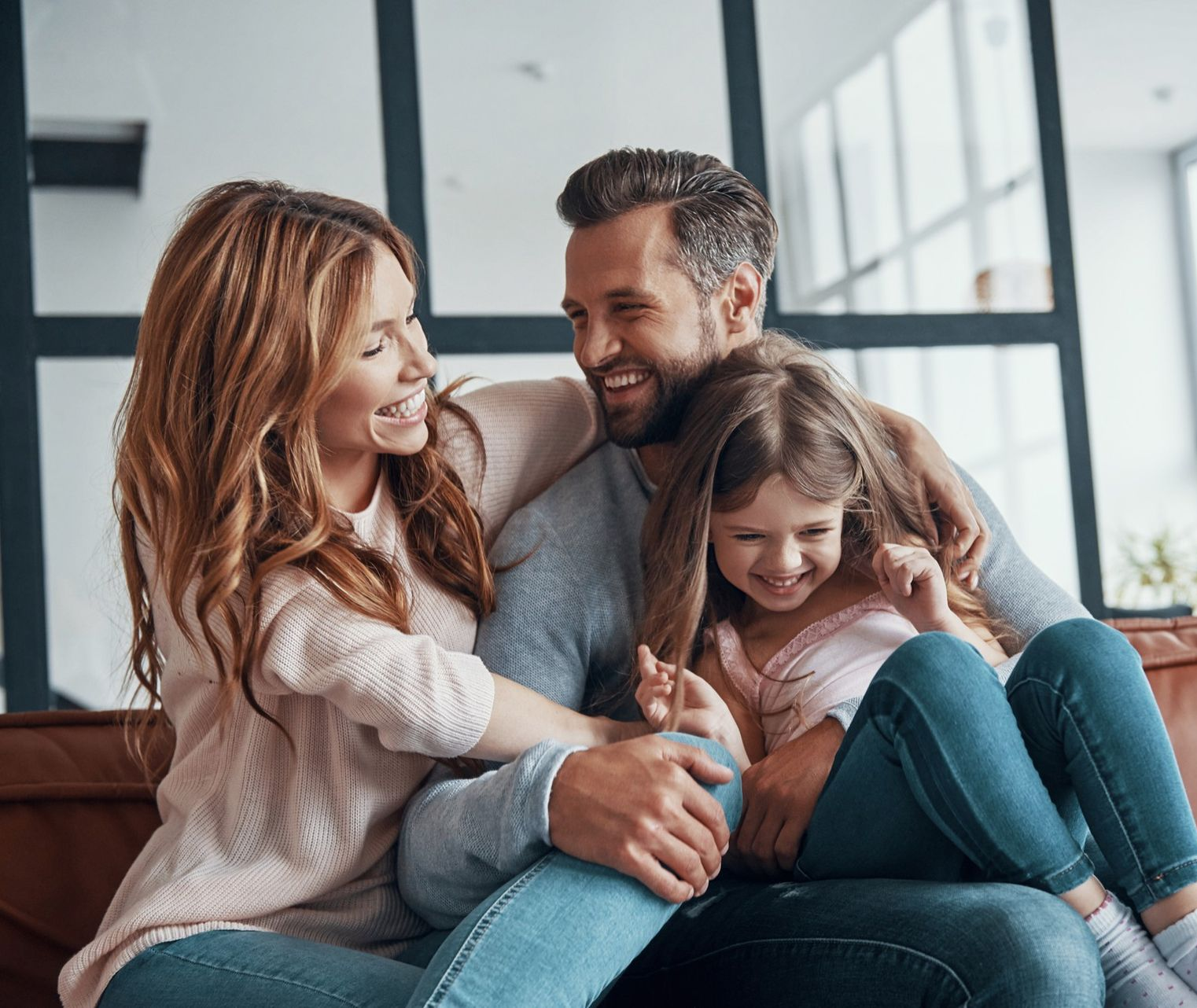 Smiling family cuddling on a couch in a bright living room