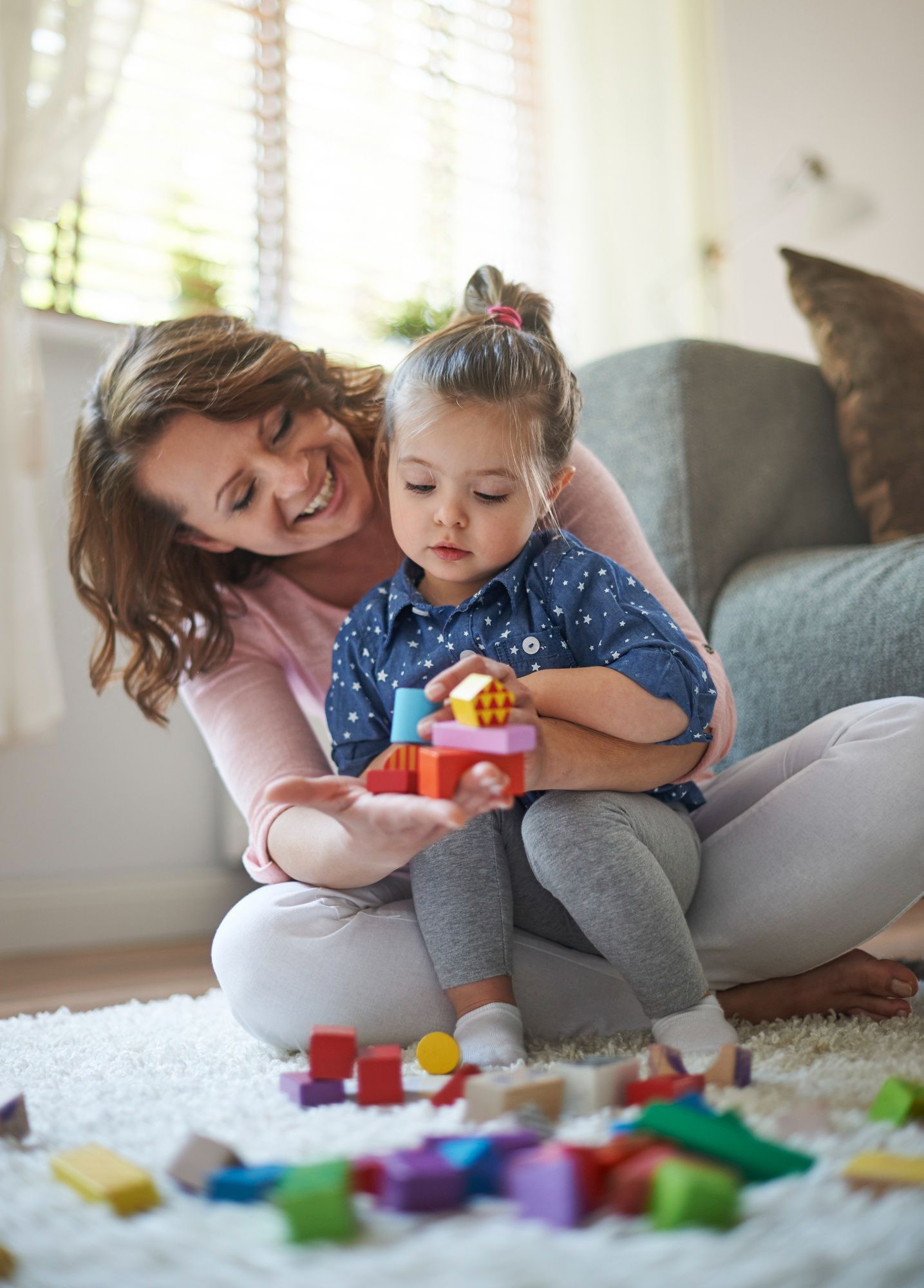 Woman and child playing with colorful blocks on a living room floor, smiling together.