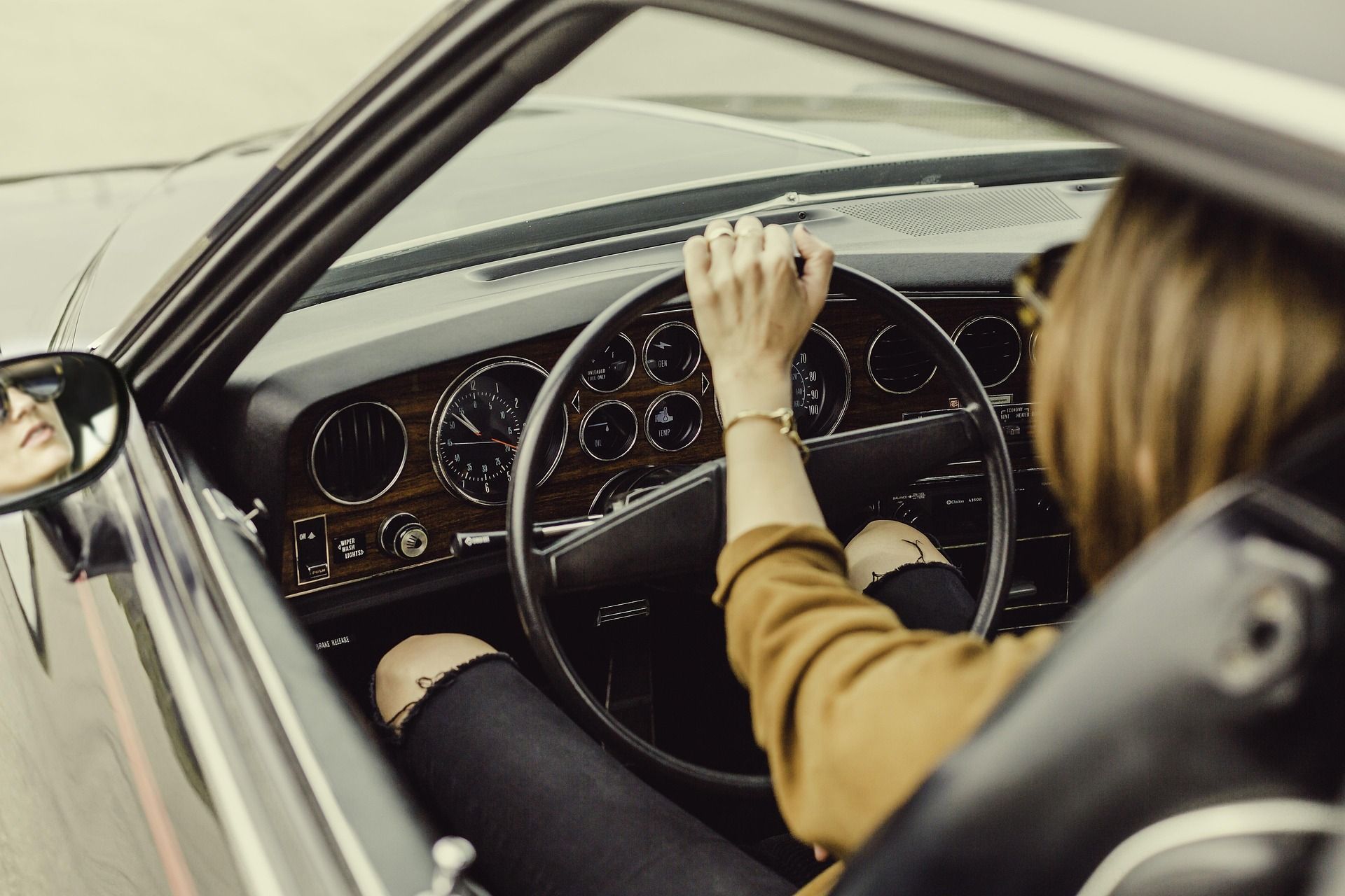 Person’s hand on a vintage car steering wheel, driving with dashboard gauges visible from the passenger side.