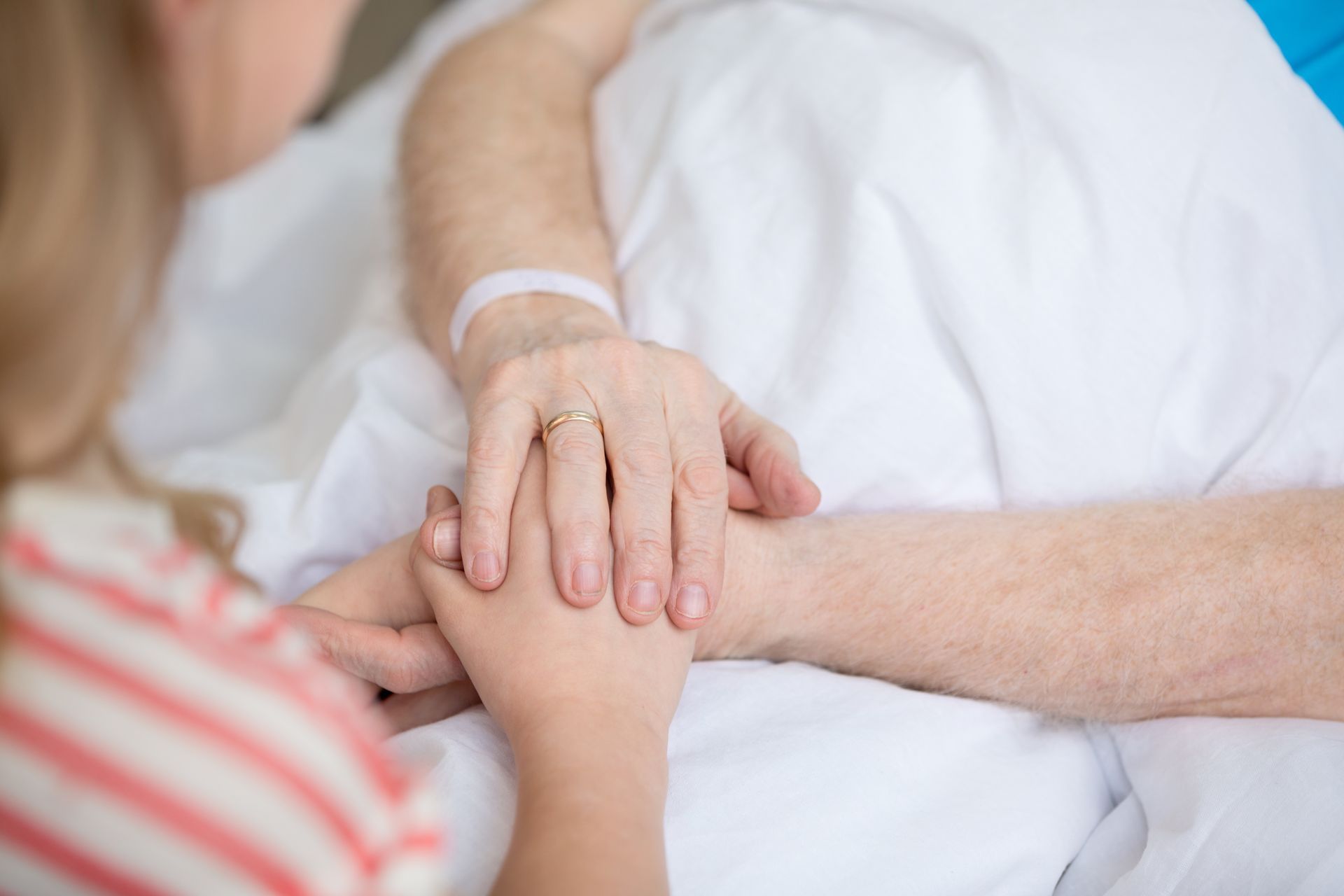 Two hands holding on a white bed, with a third hand resting supportively on top