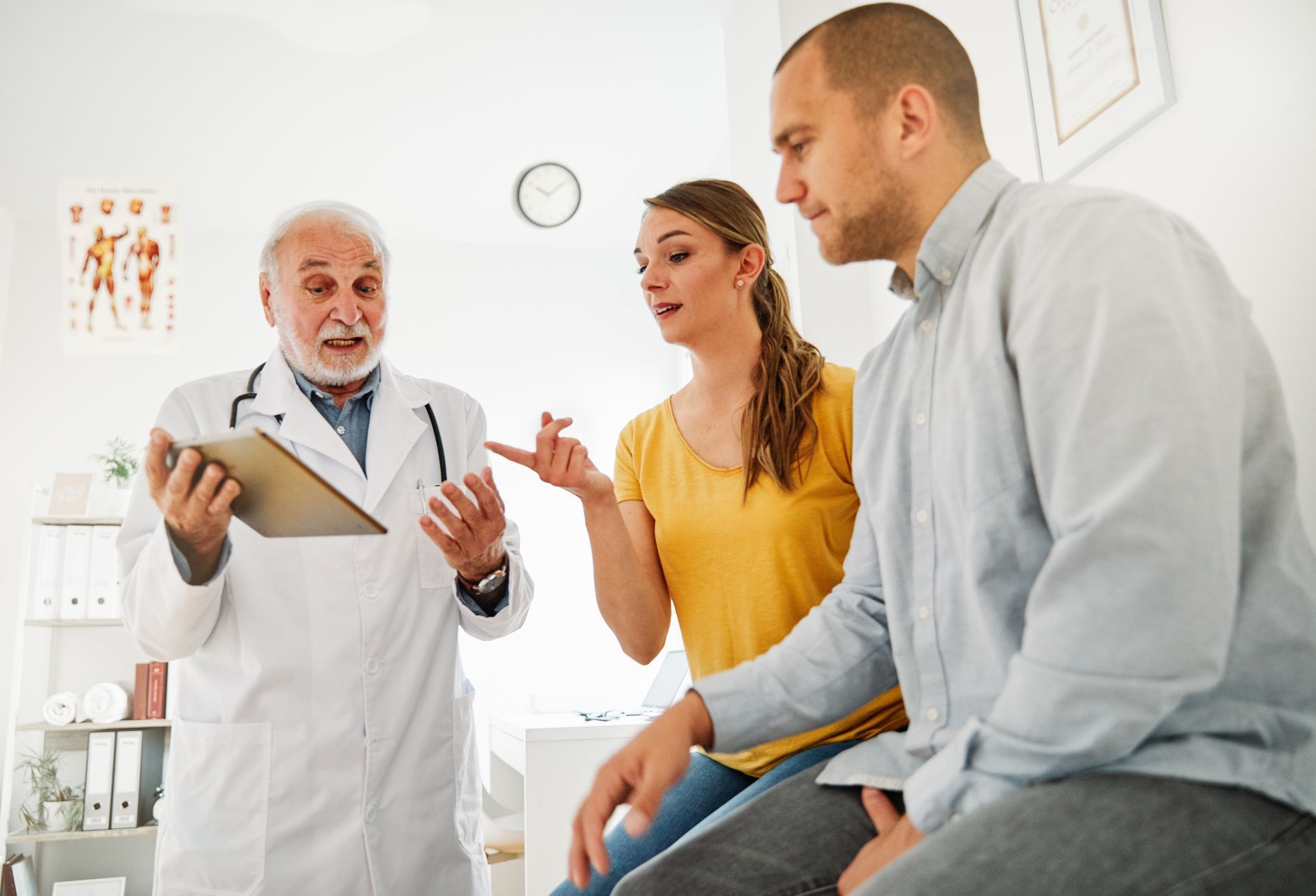 Doctor showing clipboard to seated couple in a bright clinic exam room