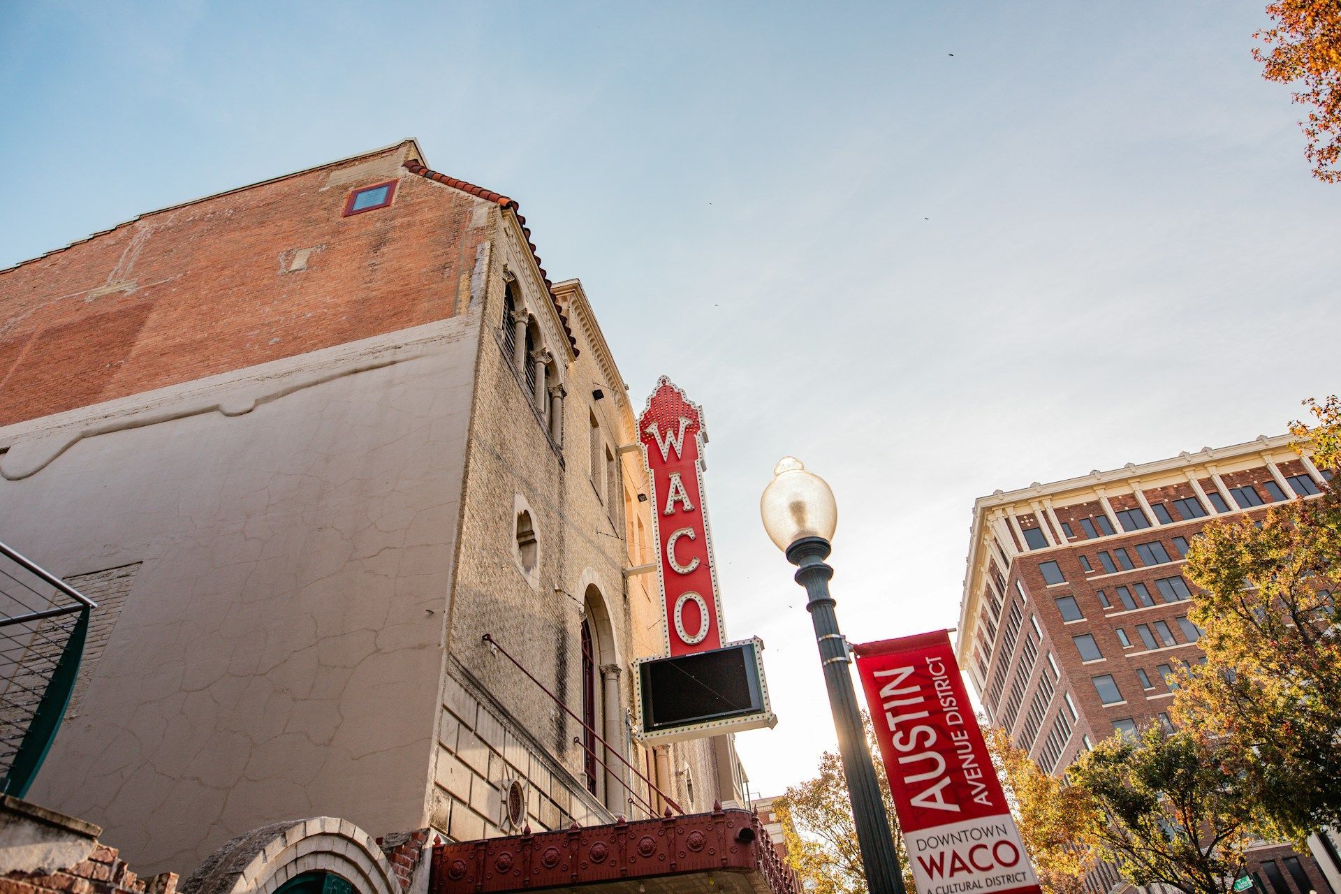 Street view of a red RICO theater sign beside a brick building and Austin street sign