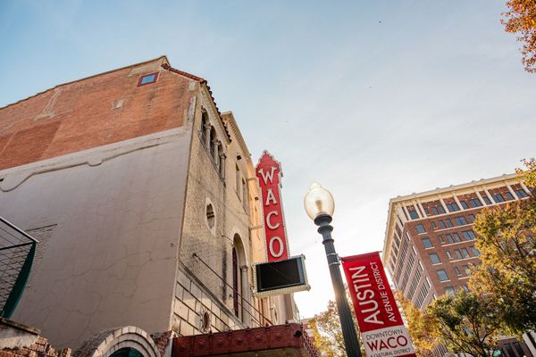Street view of a red RICO theater sign beside a brick building and Austin street sign