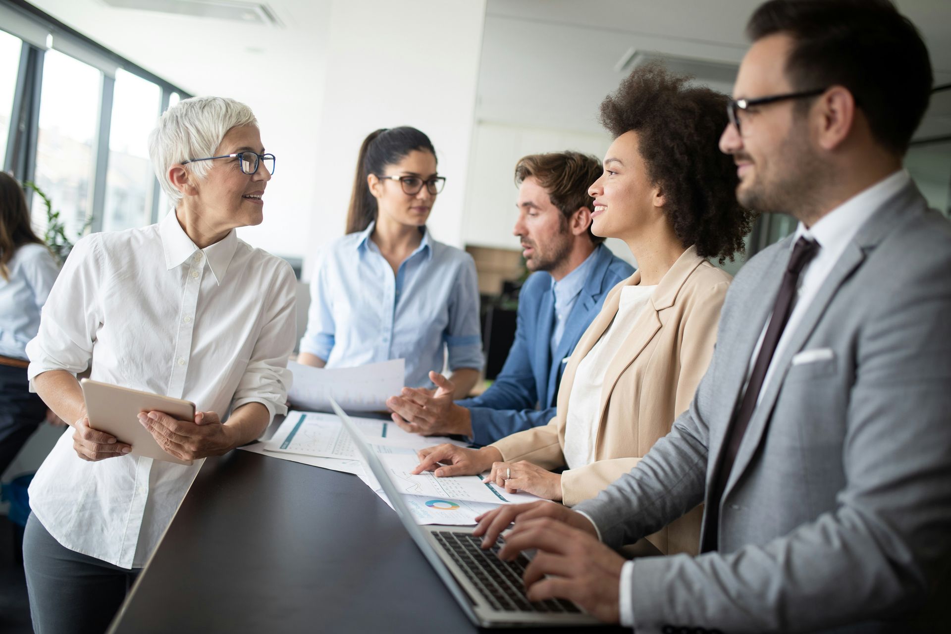 Team meeting in a bright office, with five people discussing documents around a conference table.