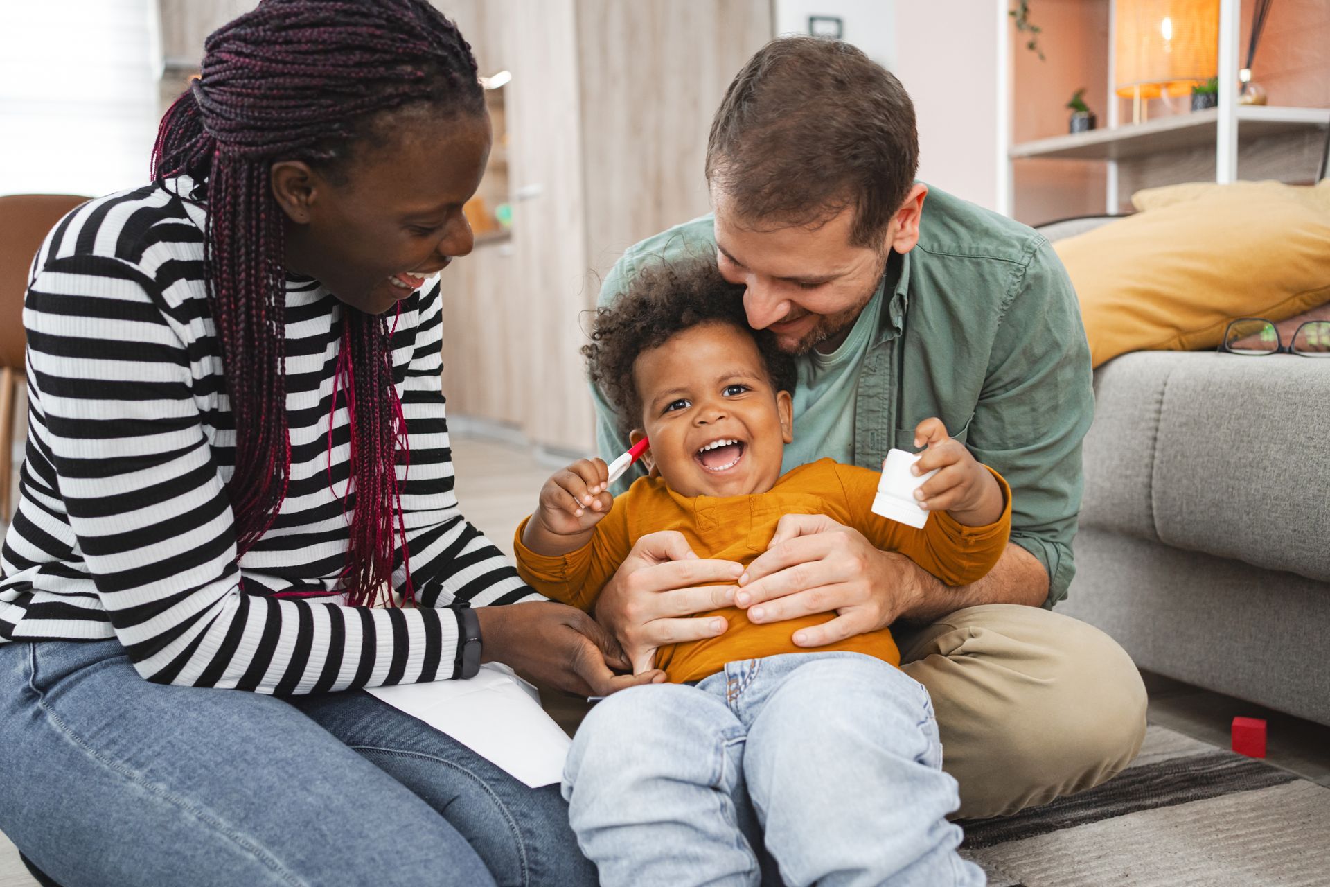 Two adults smiling and tickling a laughing child on a living room couch
