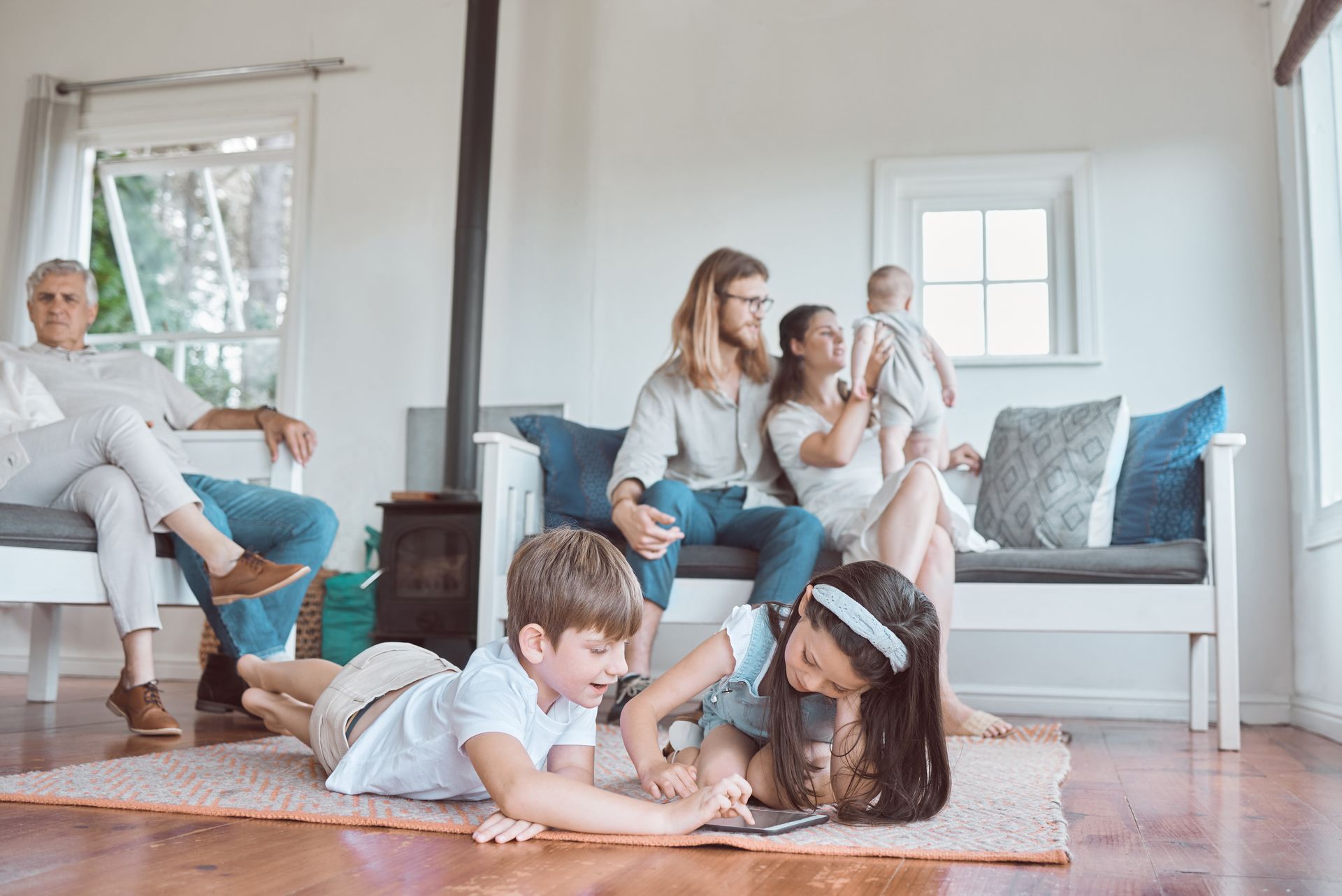 Family lounging and playing on a bright living room floor and couch with a baby and two children