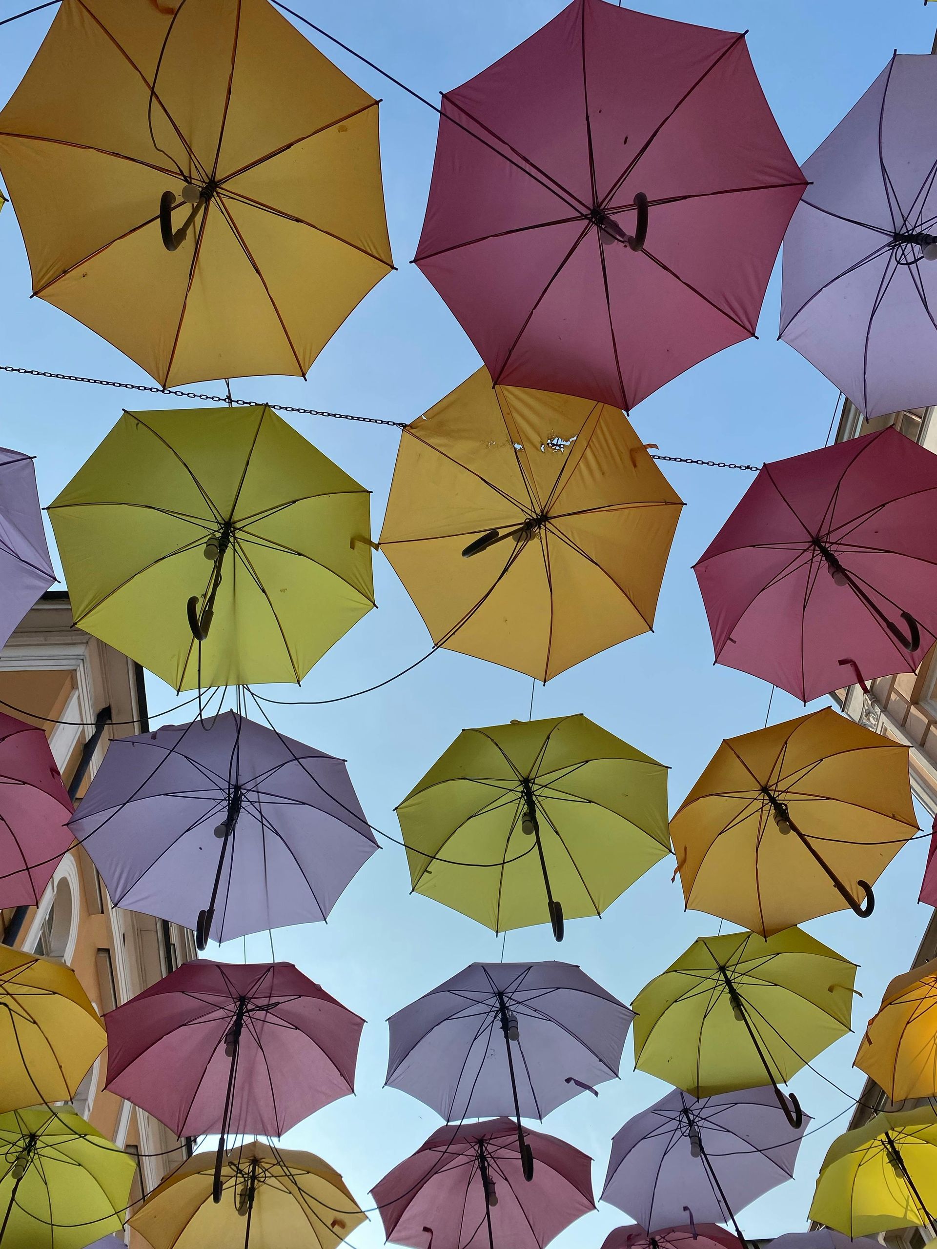Colorful umbrellas in yellow, pink, and lavender hanging overhead against a blue sky