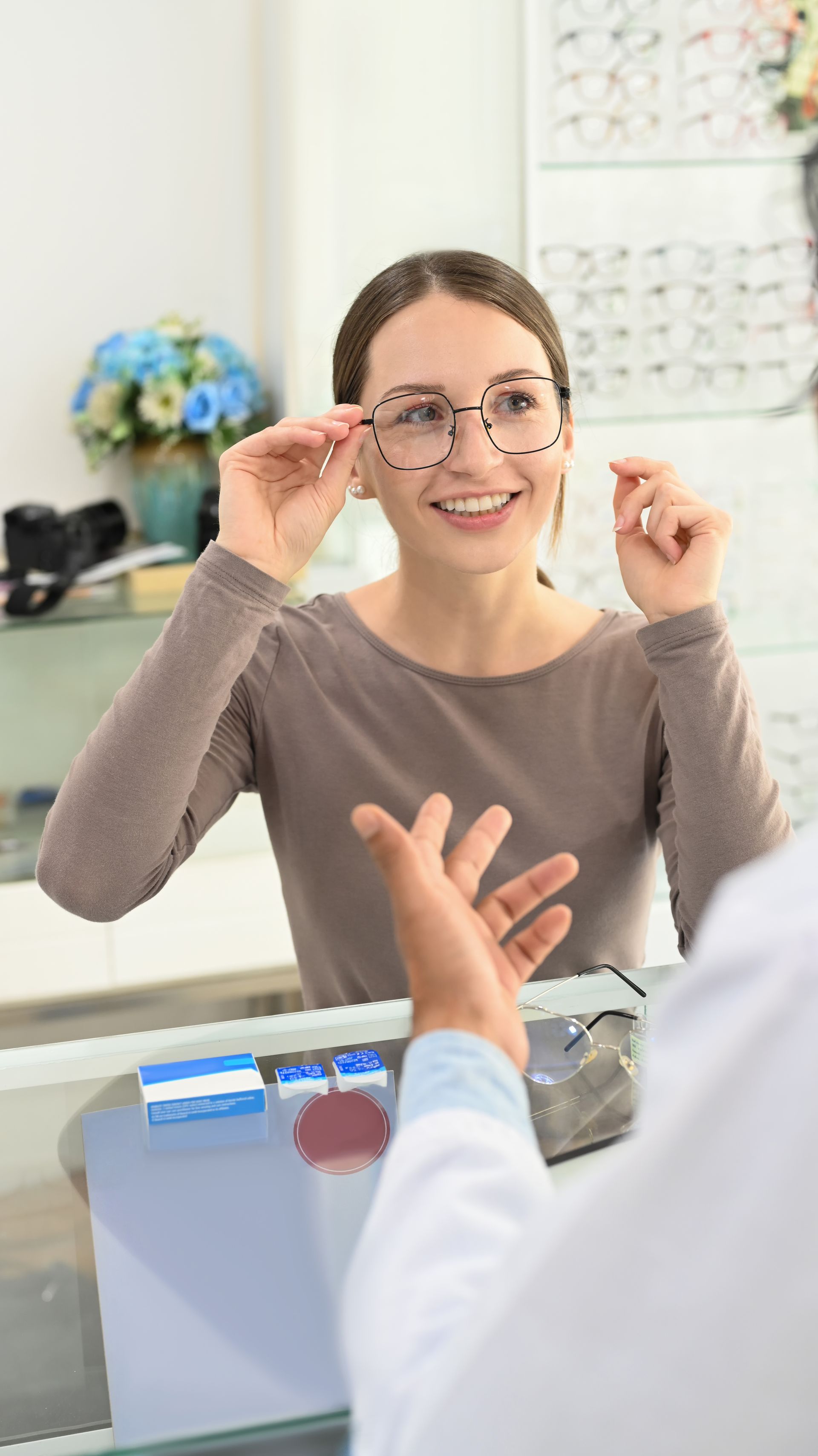 Optometrist fitting eyeglasses on a smiling patient in a bright exam room