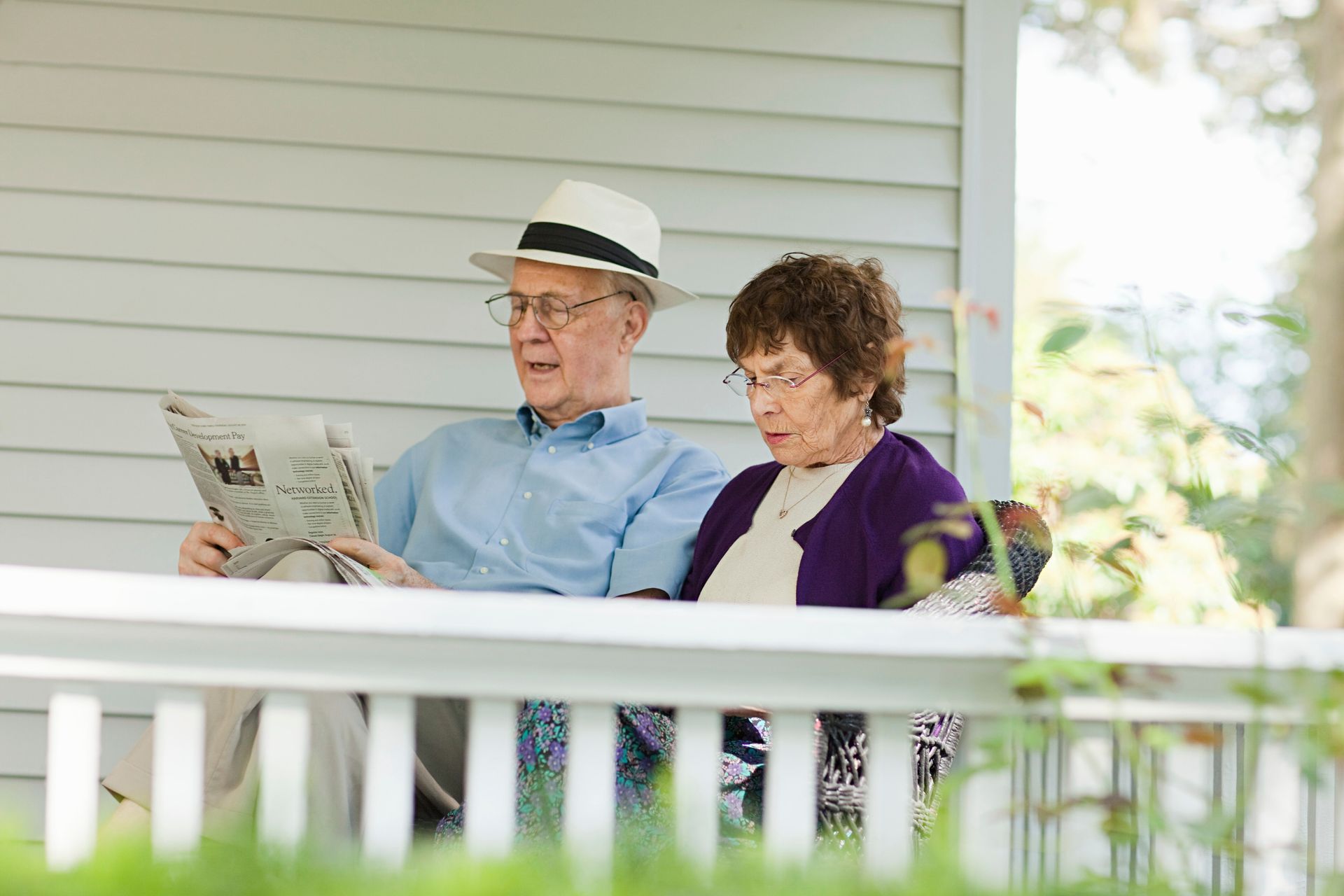 Two people sitting on a porch reading a newspaper and magazine
