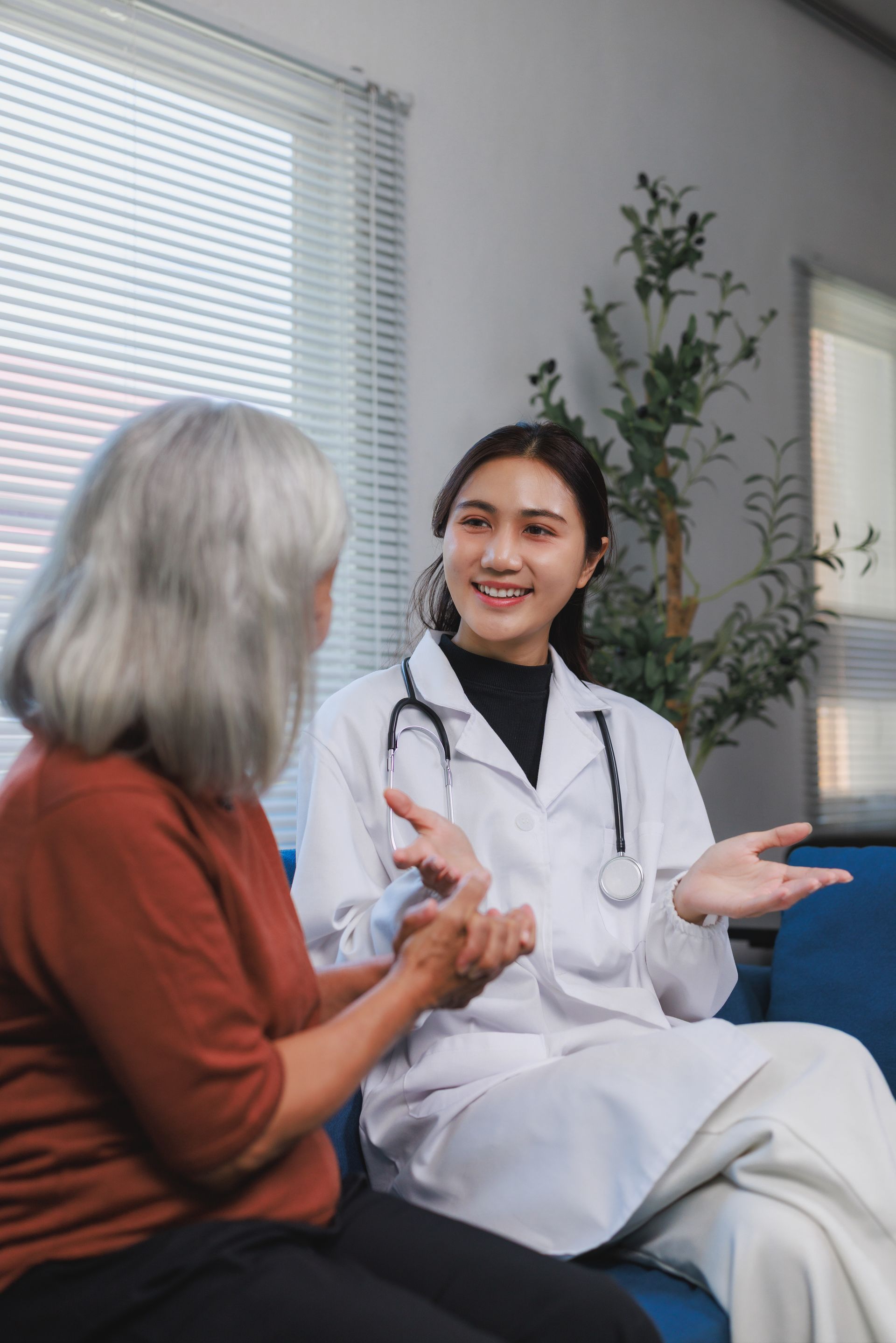 Doctor talking with a patient in a clinic, seated indoors with a stethoscope visible.