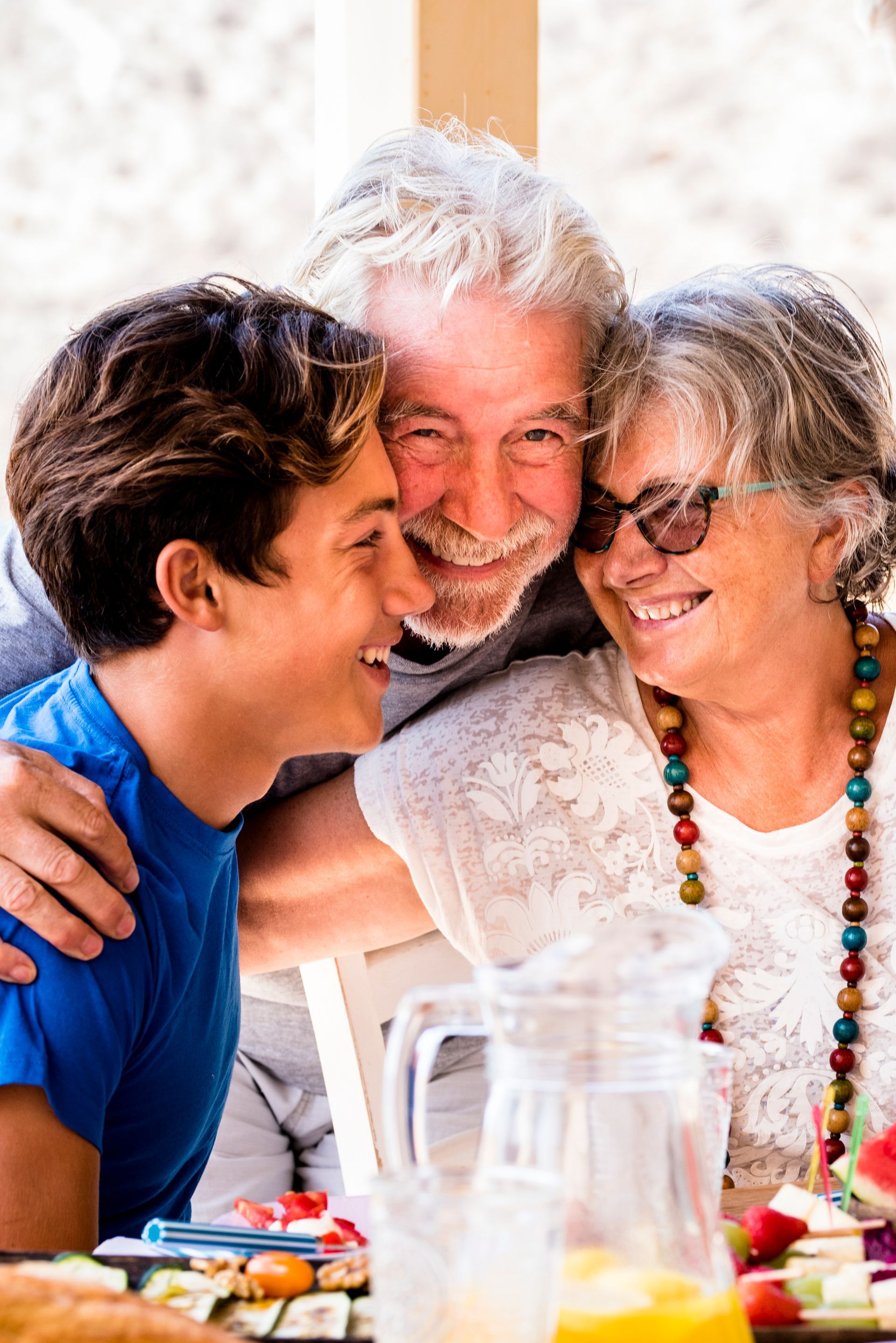 Three people smiling and embracing at a table with drinks and food outdoors
