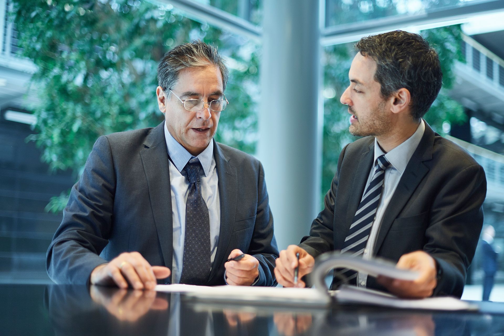 Two businesspeople in suits talking at a conference table in a bright office