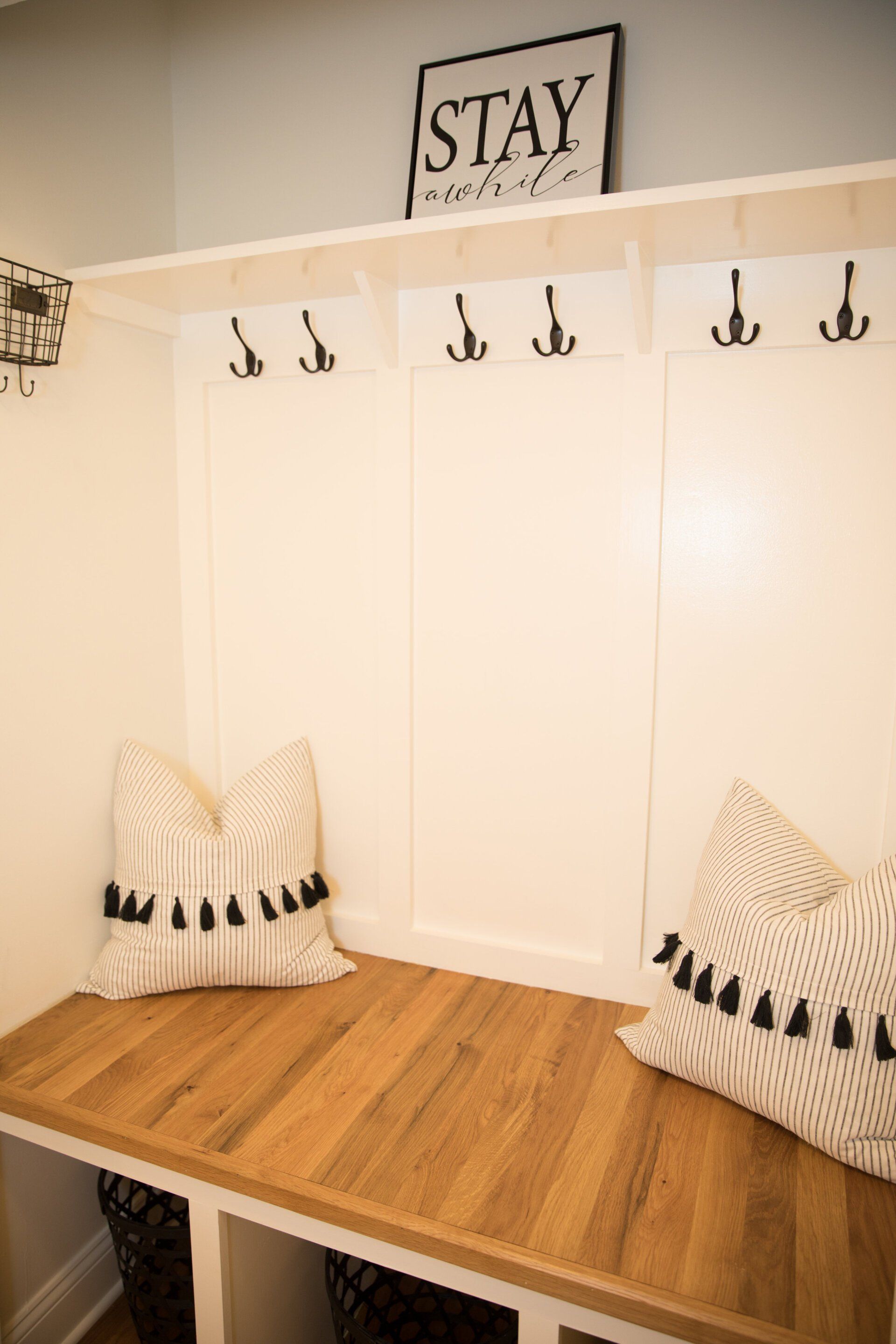 A white entryway bench with wooden seat, storage, hooks, and pillows; 