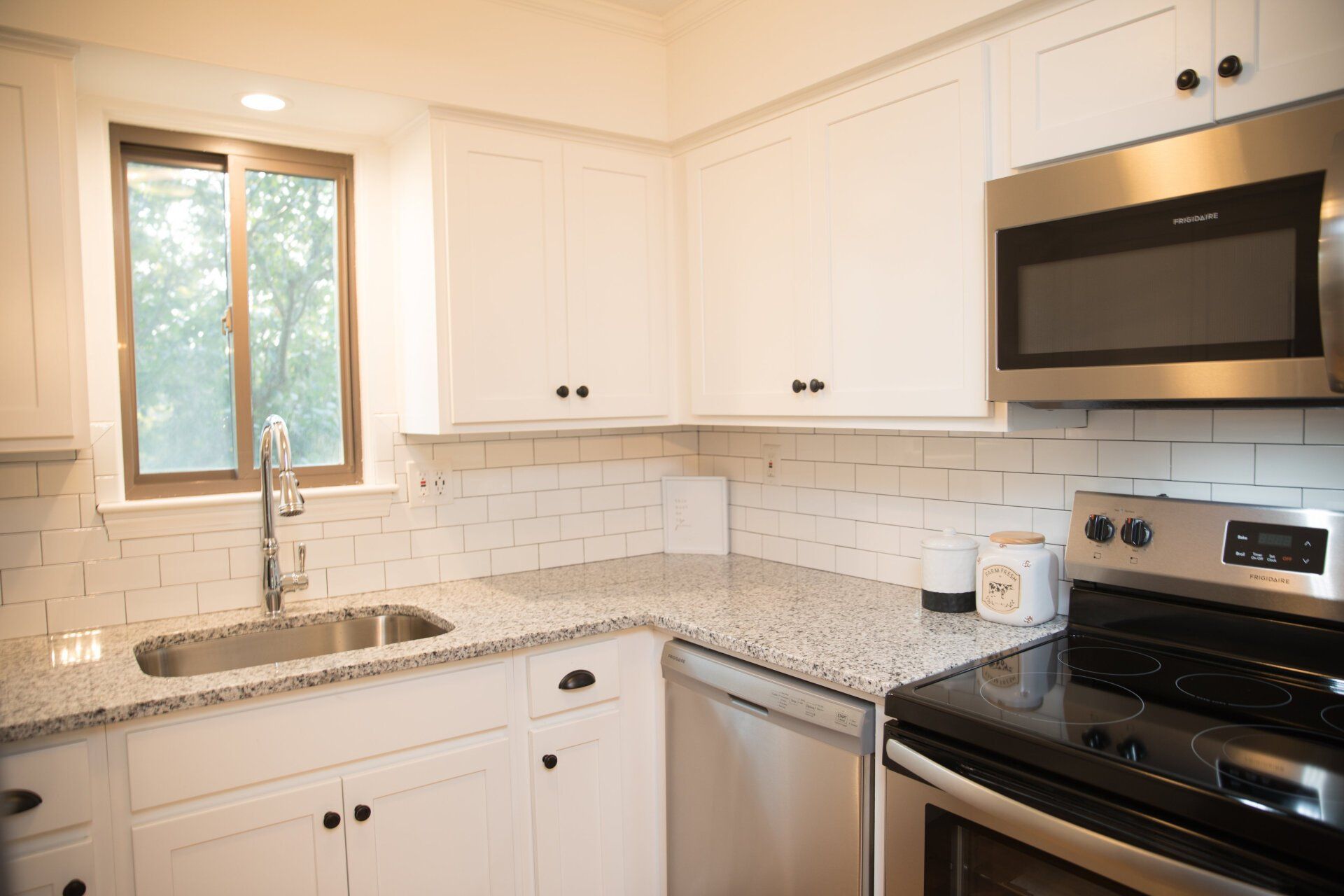 White kitchen with granite countertops, stainless steel appliances, and a window.