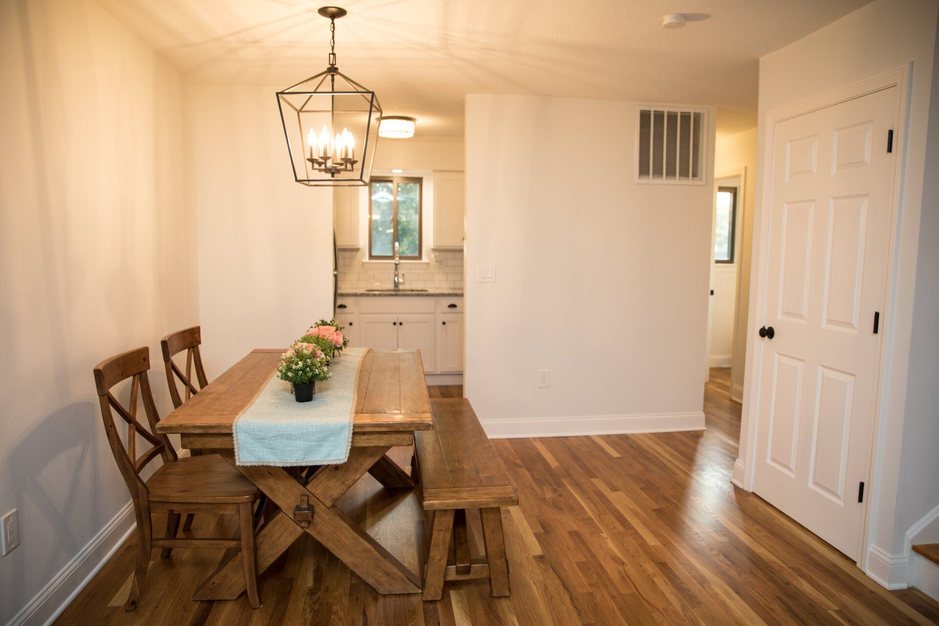 Dining room with wooden table, chairs, and bench; light fixtures, and hardwood floors.
