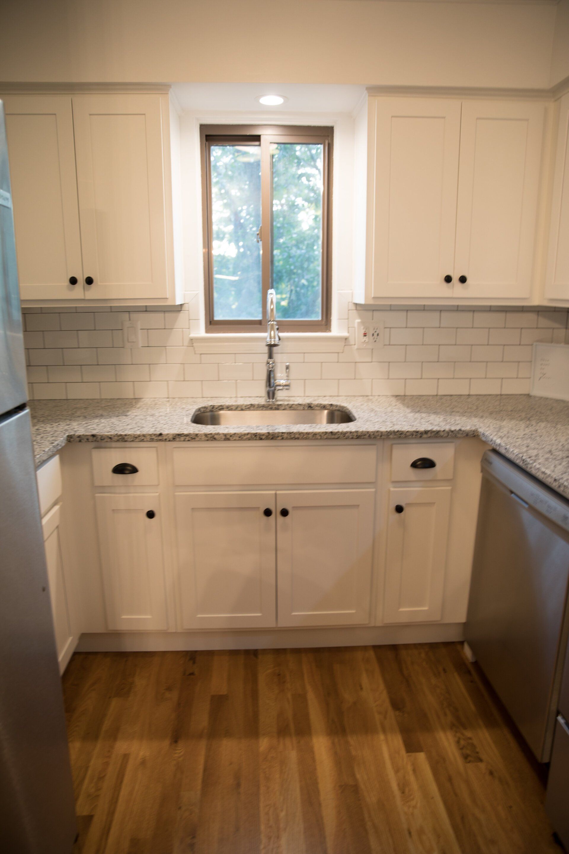 White kitchen cabinets with black hardware, granite countertops, and a window over the sink.