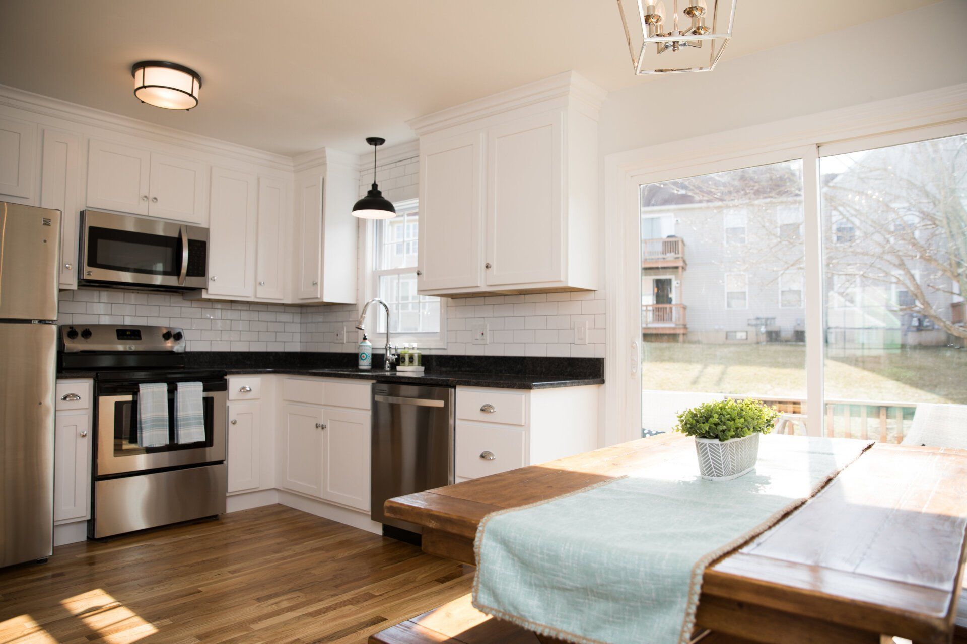 White kitchen with stainless steel appliances, wooden table, and large window.