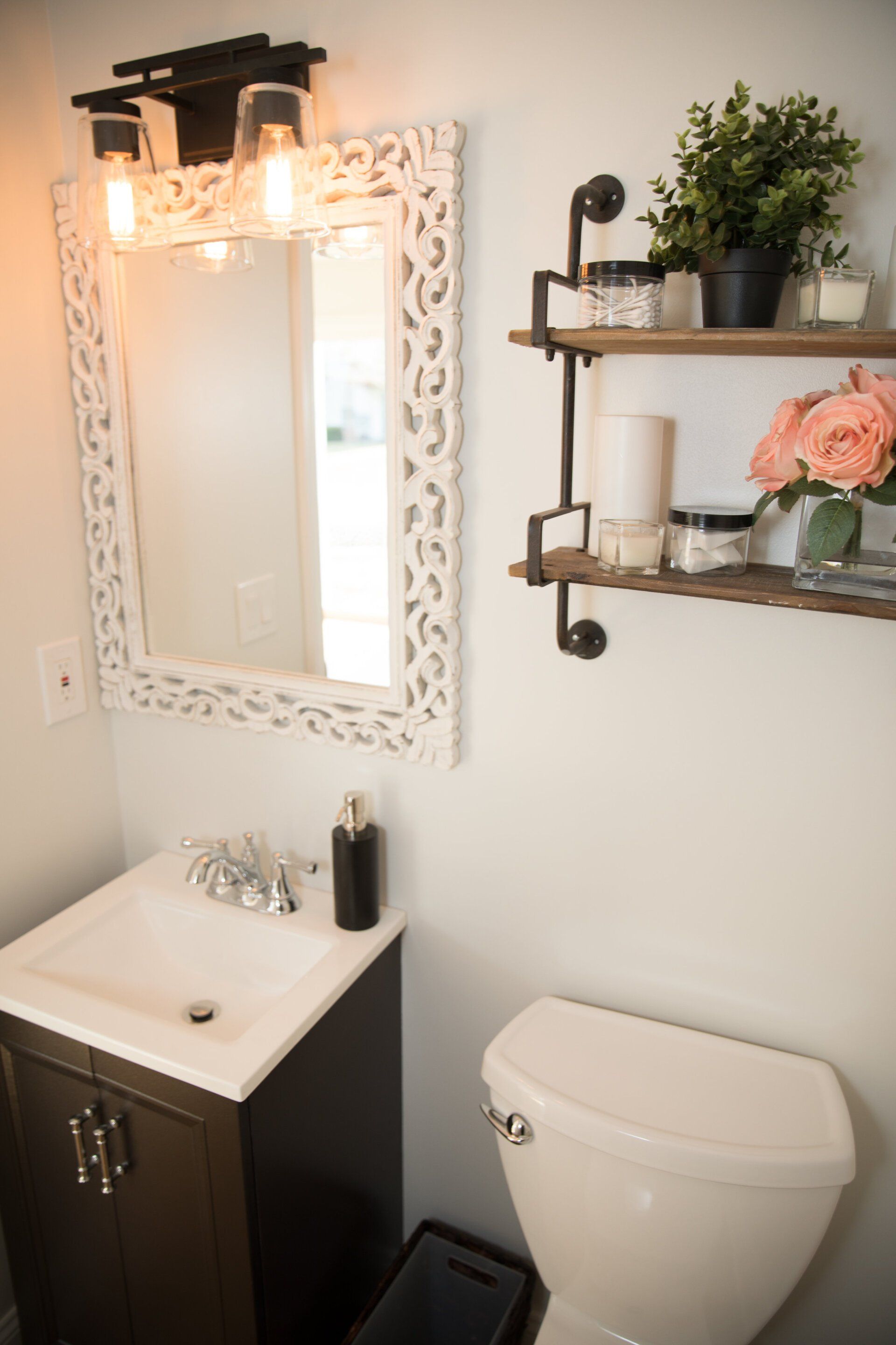 A bathroom with a vanity, mirror, toilet, and shelving, with a neutral color palette.