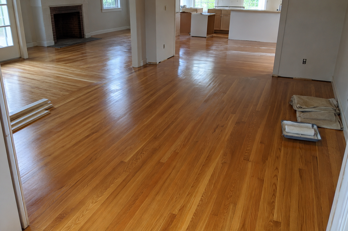 Empty living room with hardwood floors, fireplace, and open kitchen area with windows and daylight.