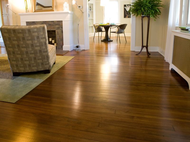 Polished hardwood floors in a well-lit living room, with a fireplace, chair, and dining area visible.