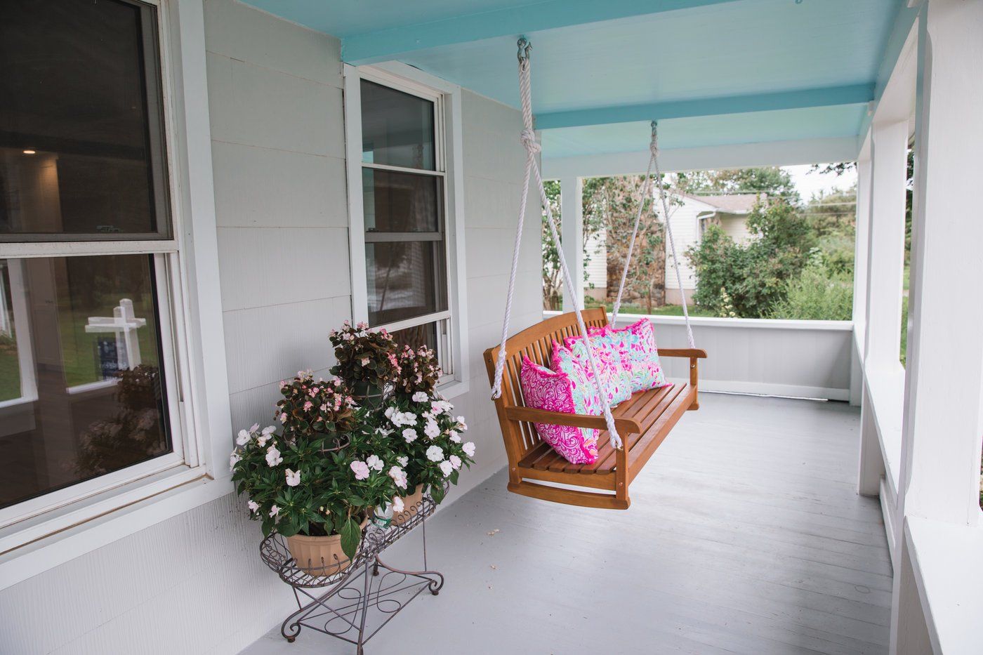Porch with a wooden swing, flowers, and blue ceiling.