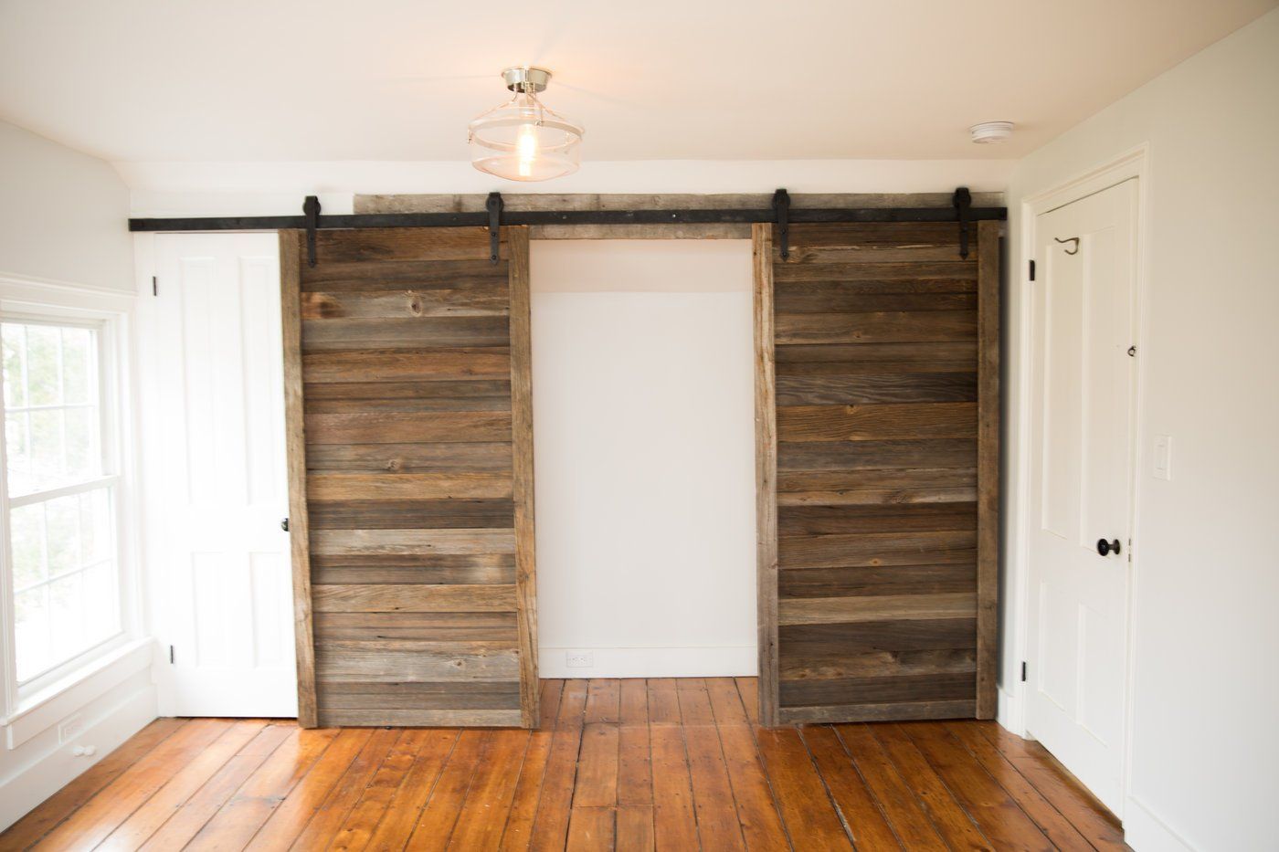 Wooden barn doors on a track, over an opening, in a room with wood floors and white walls.