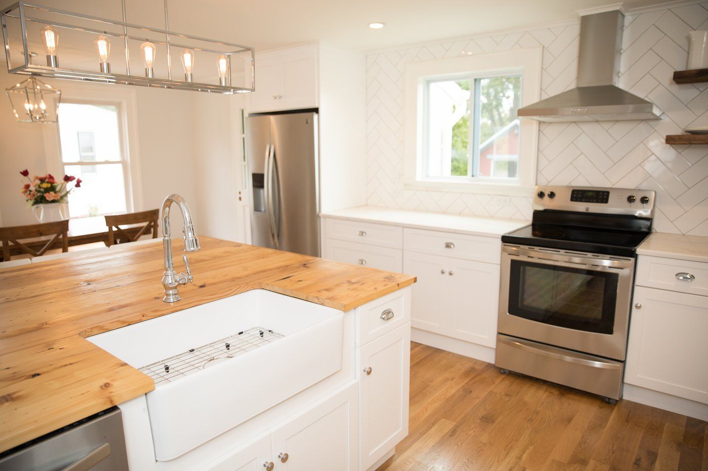 Bright, modern kitchen with a stainless steel stove, white cabinets, and wooden countertop.