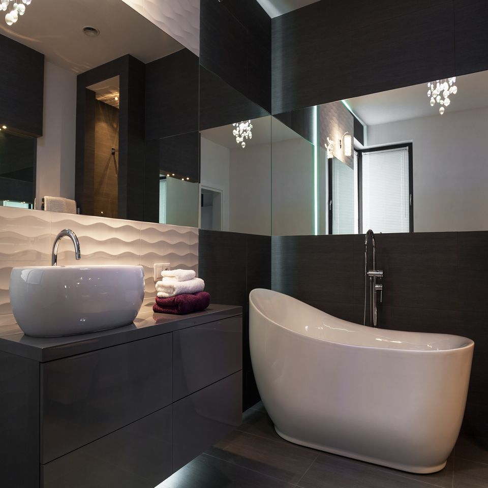 Bagno moderno in bianco e nero con vasca freestanding, lavabo a ciotola e parete a specchio.