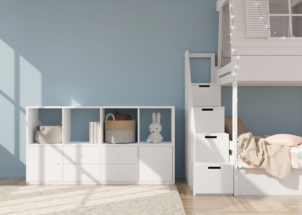 Luminosa cameretta per bambini con scaffali a cubo bianchi, letto a soppalco con scaletta, peluche e pareti azzurre.