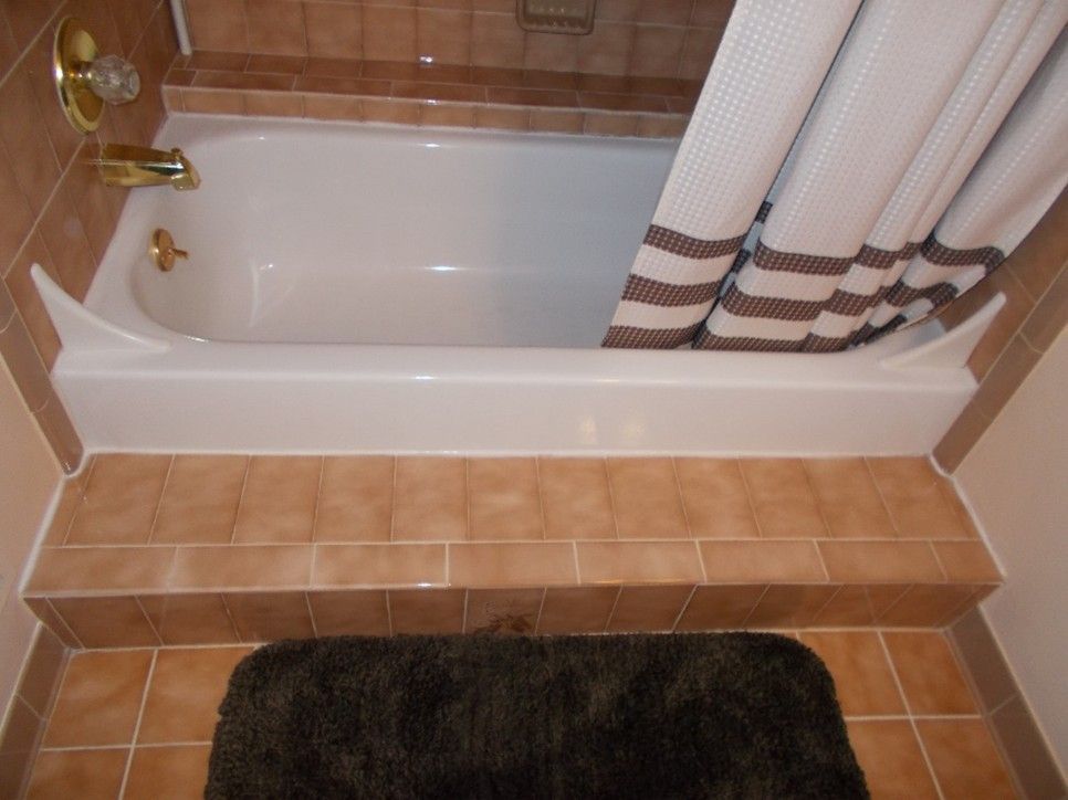 White bathtub with tan tile surround, shower curtain, and a dark brown bath mat.