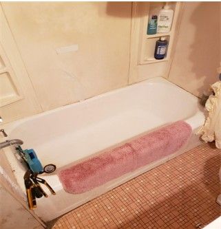 White bathtub with pink mat, toiletries in wall niche, brown and pink tiled floor.