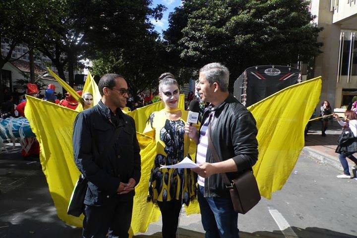 Dos hombres entrevistan a una persona vestida de amarillo al aire libre.