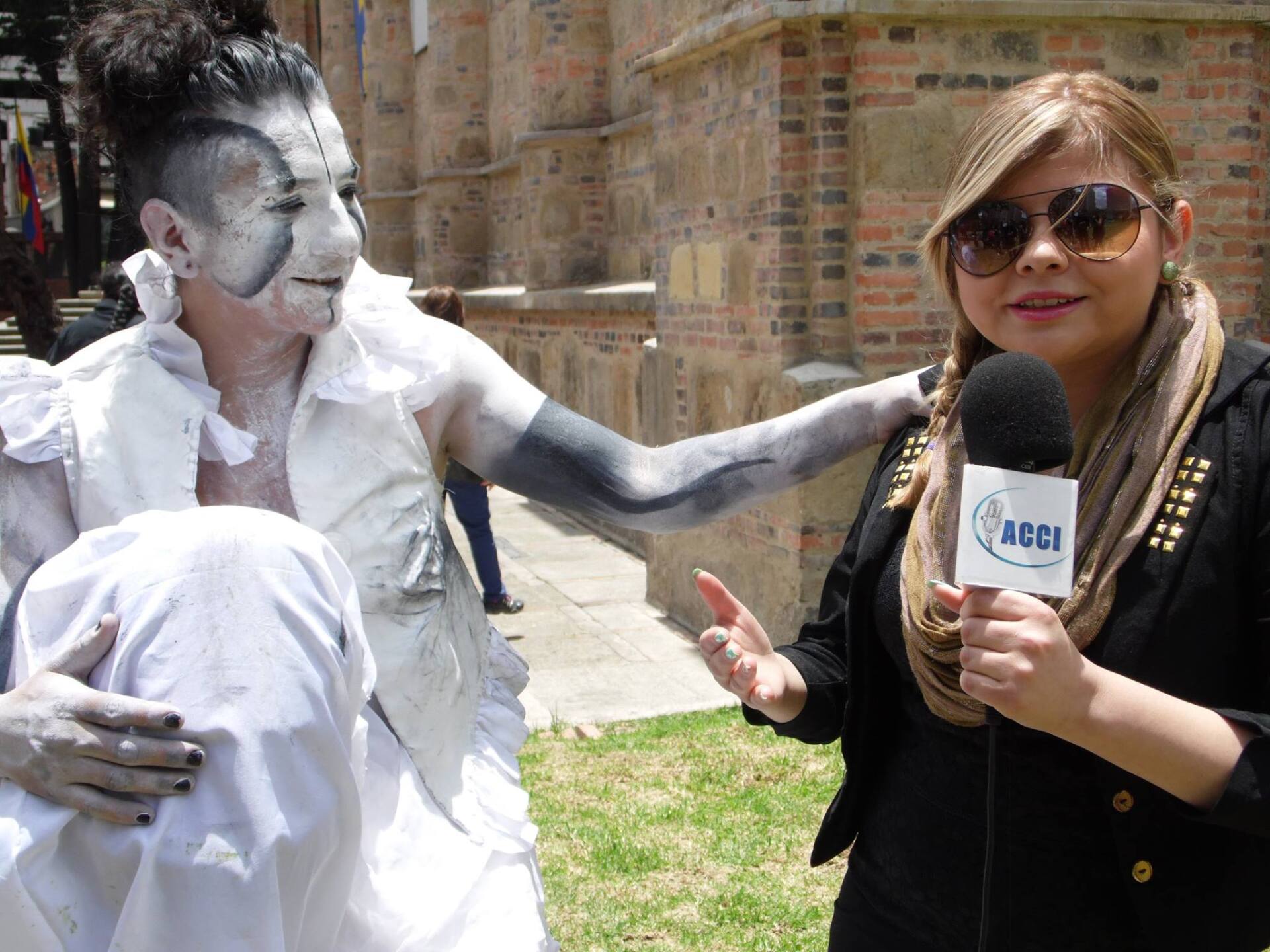 Un reportero entrevista a una persona con pintura corporal blanca afuera de un edificio con patio.