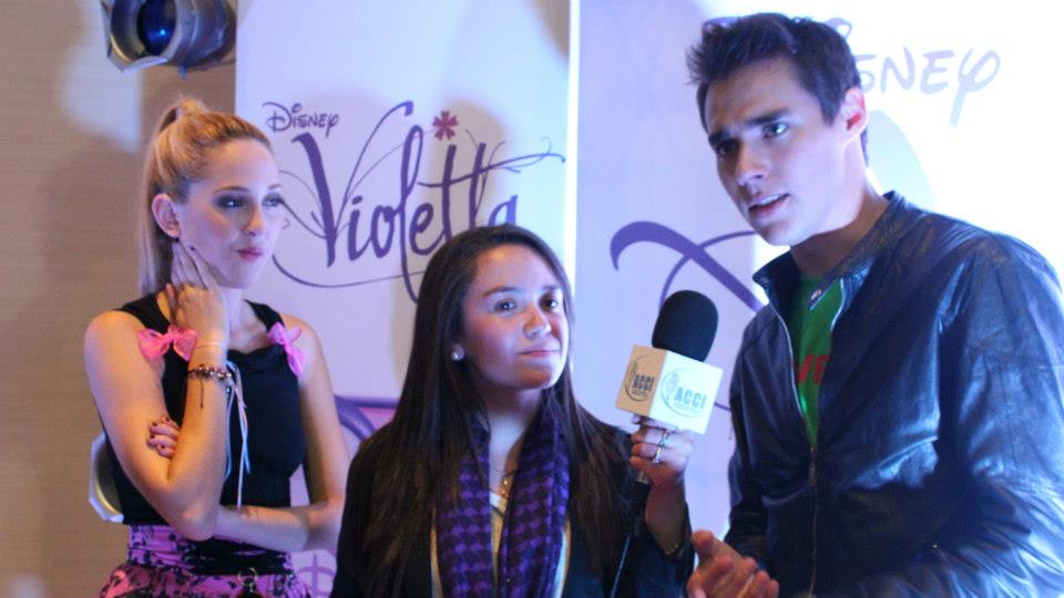 Mujer y hombre siendo entrevistados en un evento de Violetta de Disney; fondo morado, micrófono.