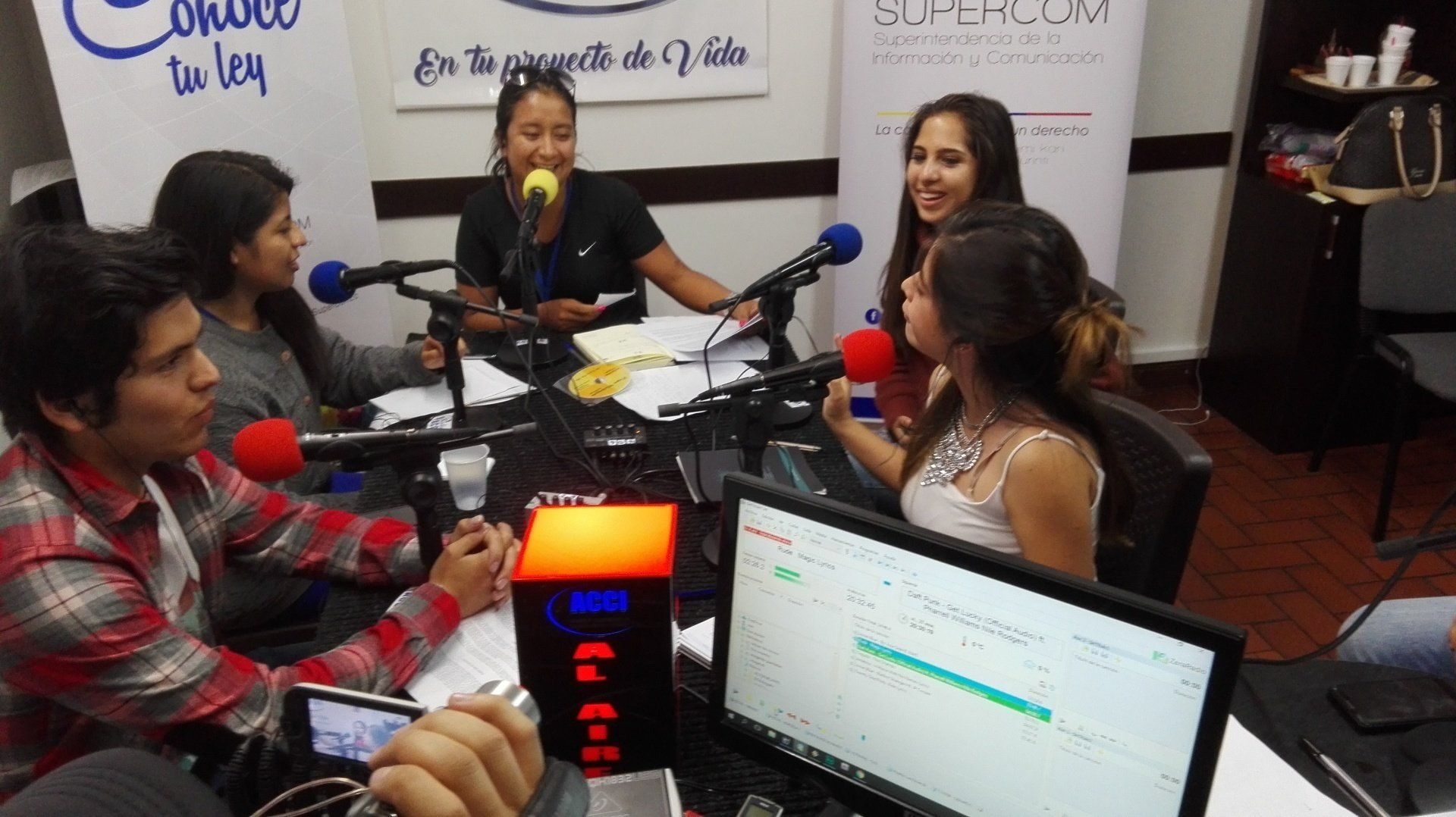 Personas alrededor de micrófonos en un estudio de radio; discutiendo.