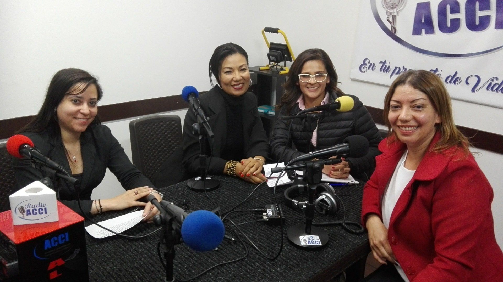 Cuatro mujeres sentadas en una mesa con micrófonos, posiblemente para la grabación de un podcast, en un estudio.