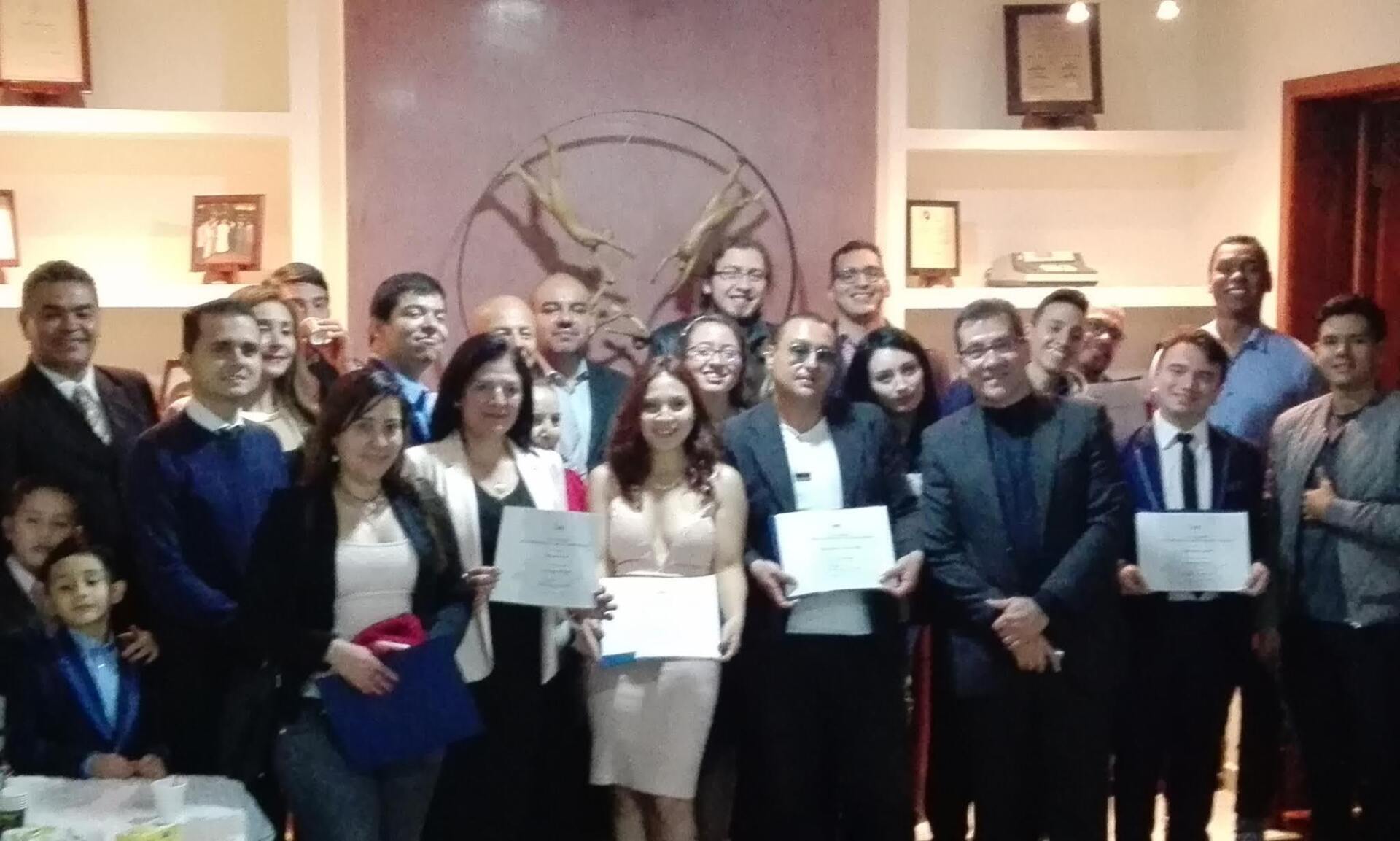 Grupo de personas sosteniendo certificados, sonriendo, en el interior con decoraciones.
