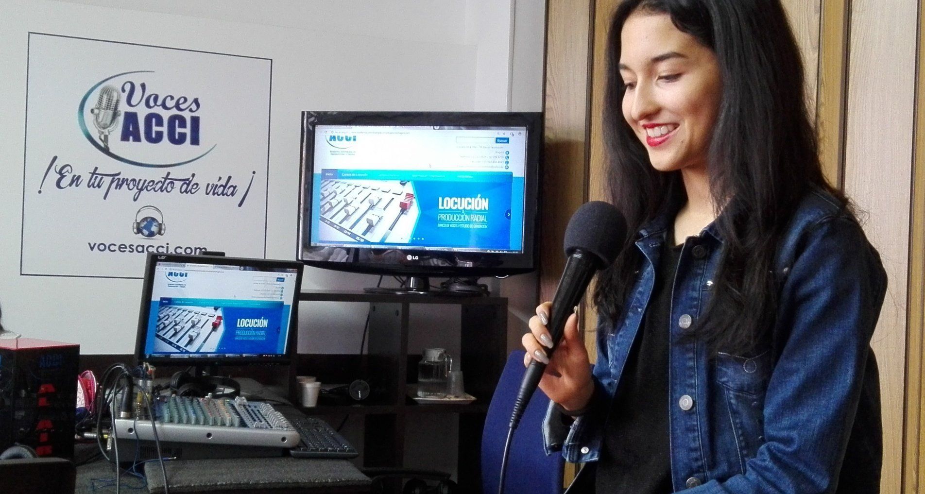 Mujer sonriendo con un micrófono en un estudio de radio. Computadoras y un logotipo al fondo.