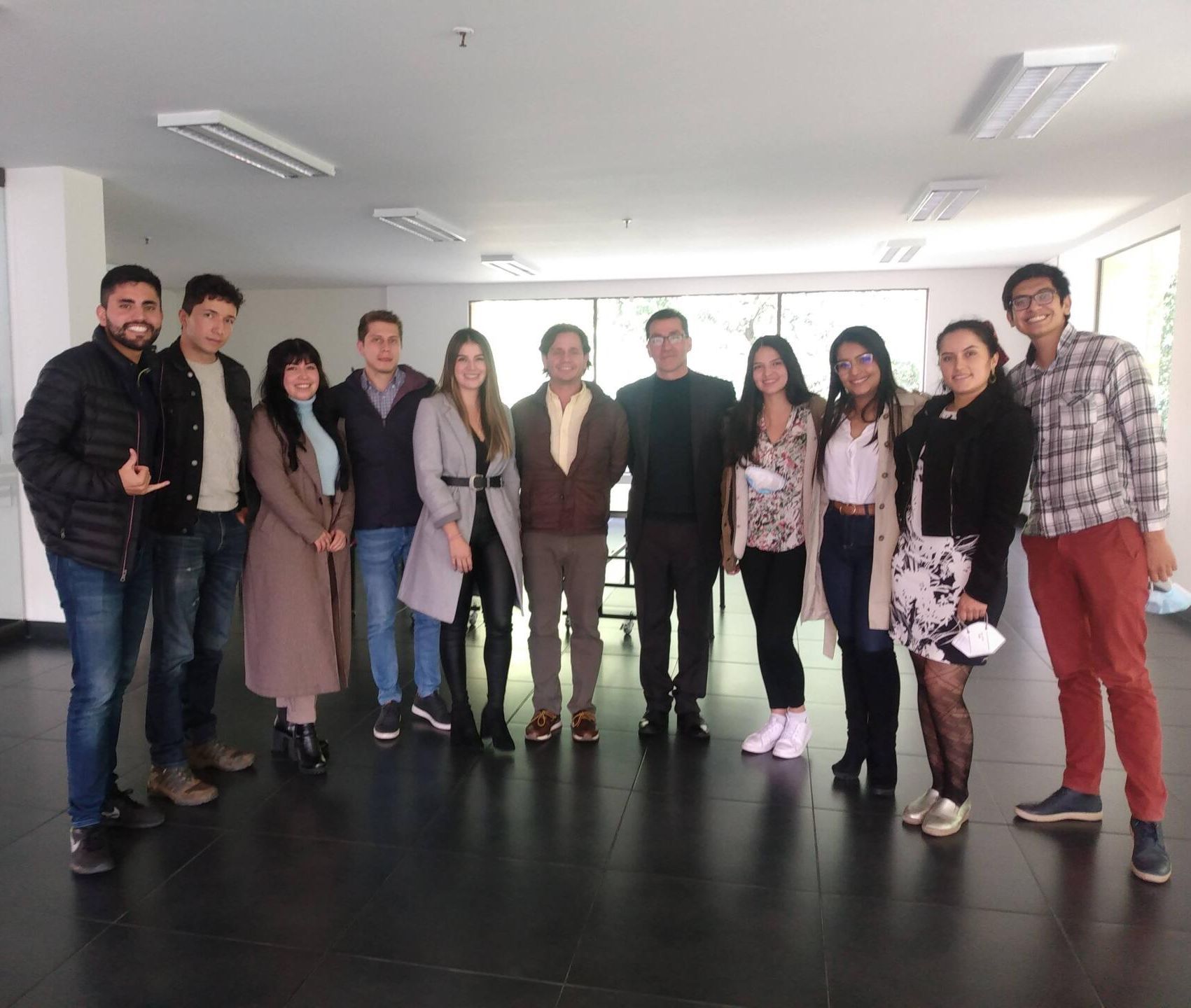 Grupo de personas de pie en una habitación con paredes de colores neutros y suelo oscuro, posando para una foto.