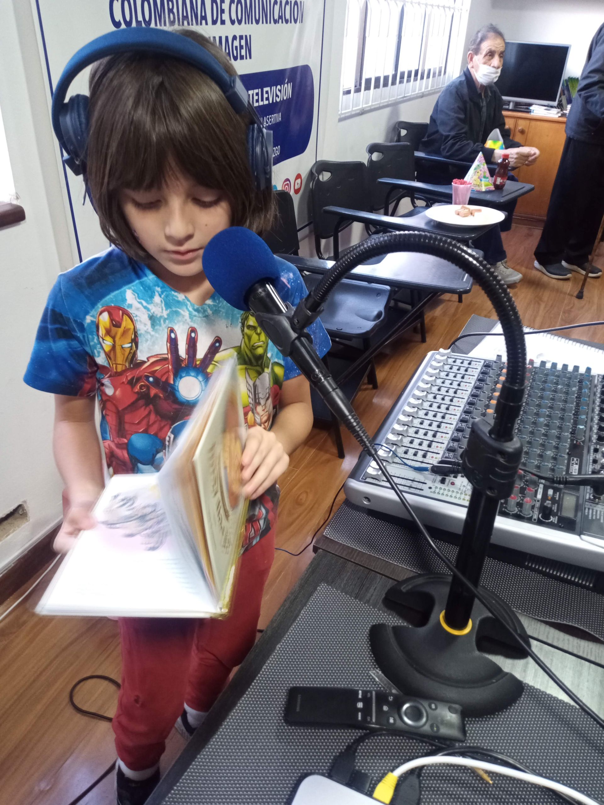 Un niño con auriculares lee un libro a través de un micrófono en un estudio de radio.